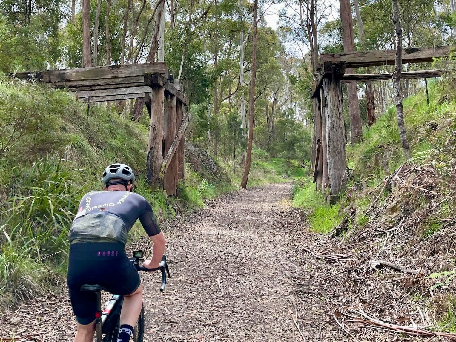 Cyclist riding on smooth gravel road with a unused timber railway bridge and native bushland in the background