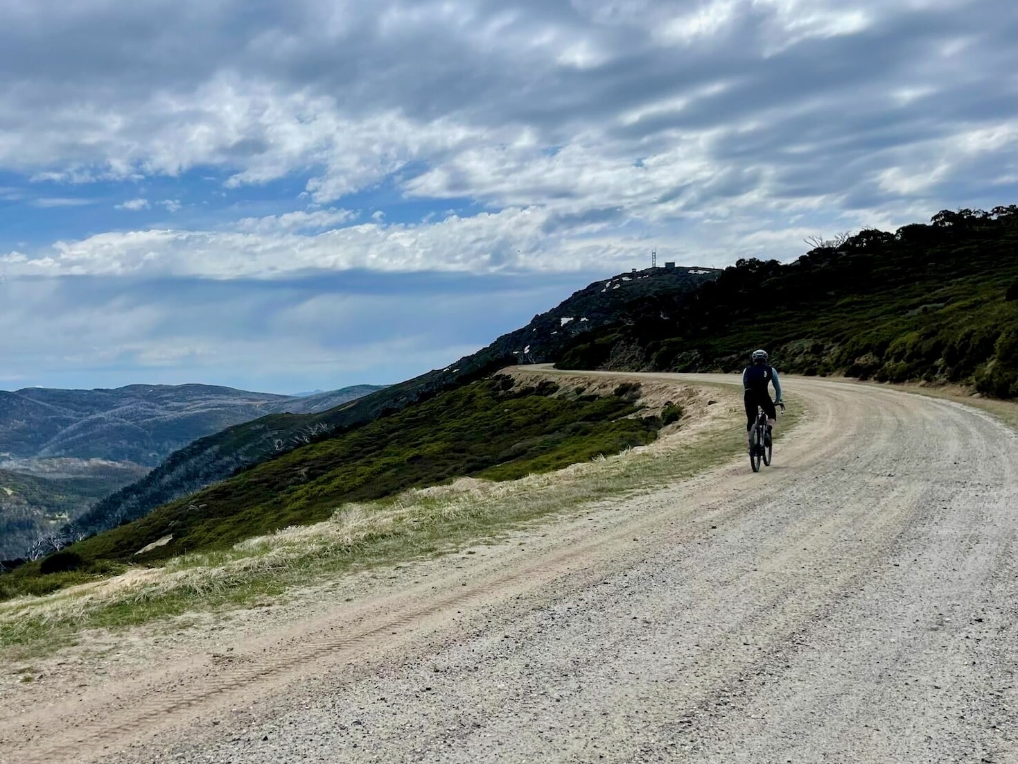 Cyclist riding along an Alpine gravel road with views of the surrounding mountains and valleys on a sunny day