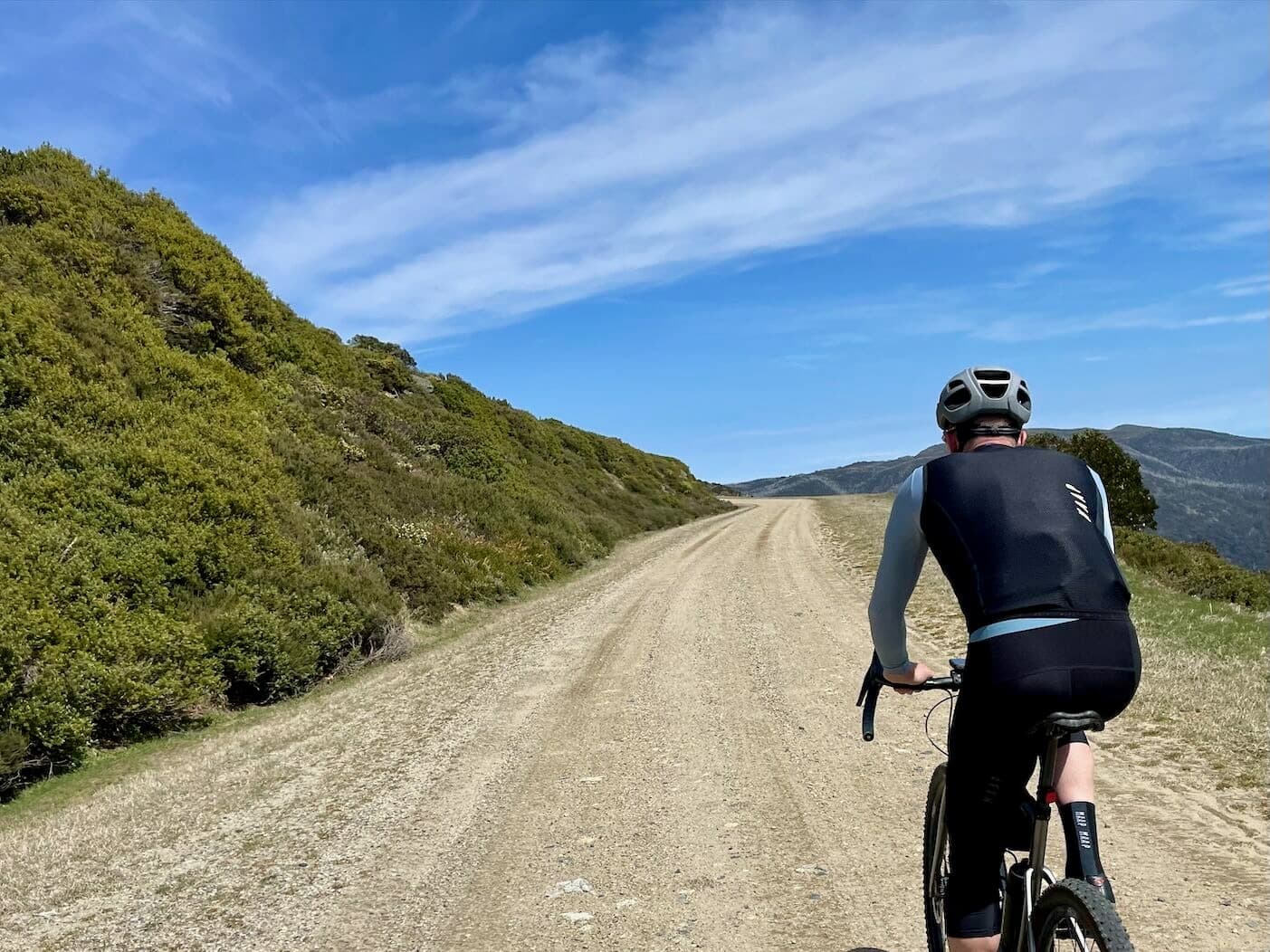Cyclist riding up a smooth gravel road leading to the summit of Mt McKay  with views of surrounding mountains and valleys on a sunny day