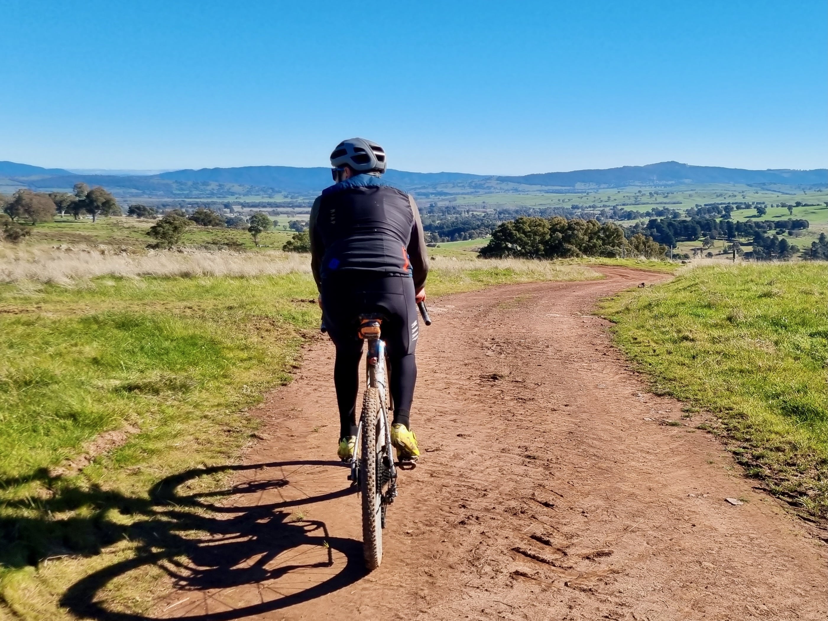Cyclist riding on a smooth gravel road with rolling hills in the distance on a sunny day