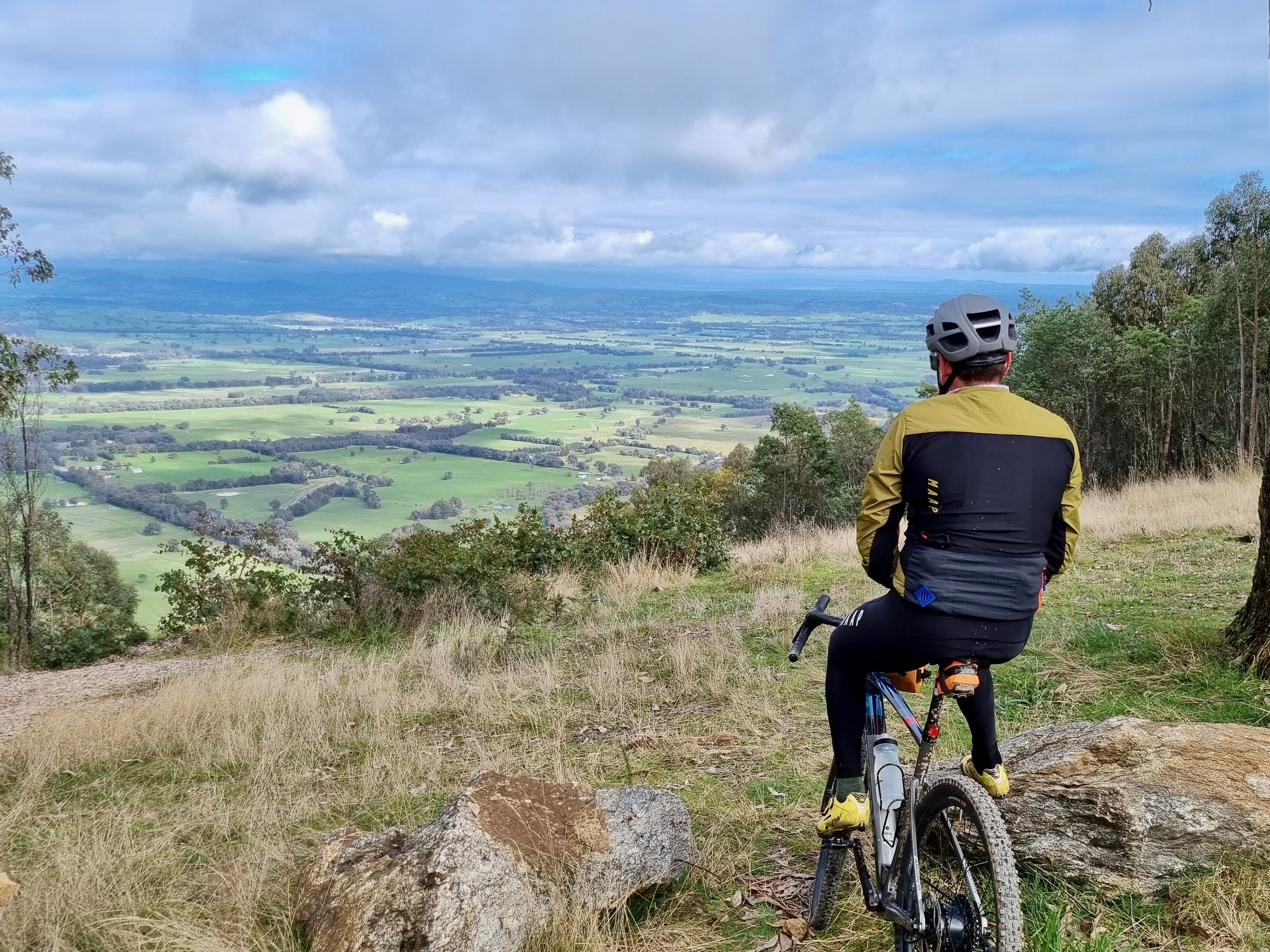 A cyclist stopped at the Murmungee lookout looking at the view of the surrounding valley and mountains off in the distance on a sunny day