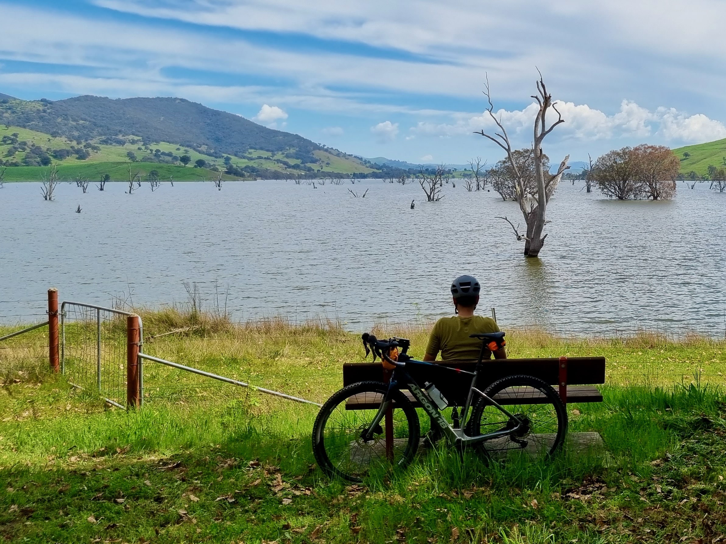 Cyclist sitting on a park bench on the edge of lake enjoying the view