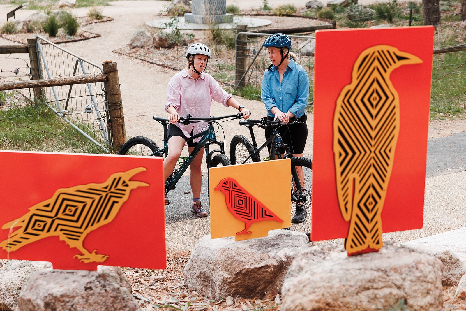 Two female cyclists looking at outdoor indigenous artworks of native animals