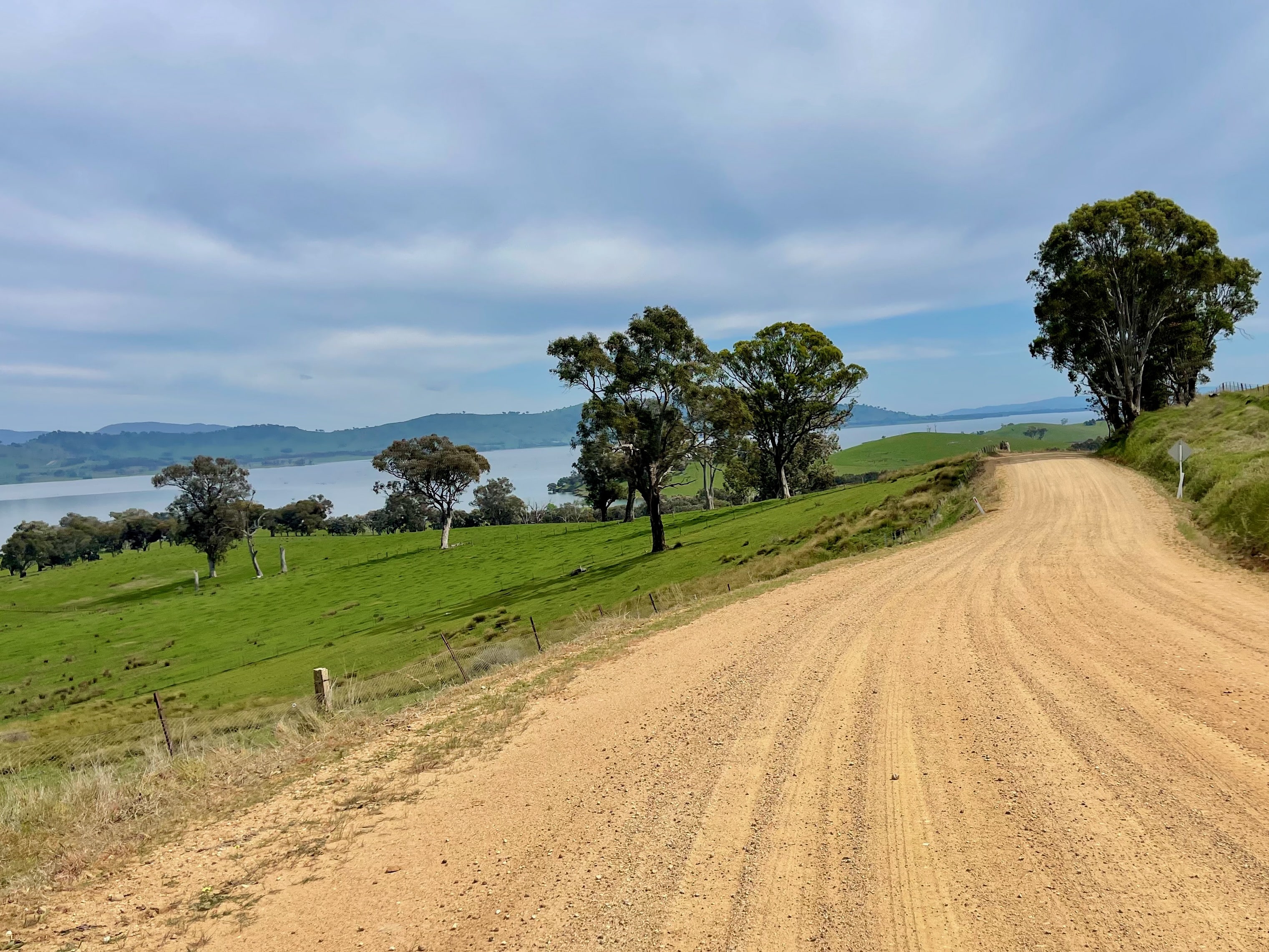 Gravel road winding through open farmland with views of lake in the distance