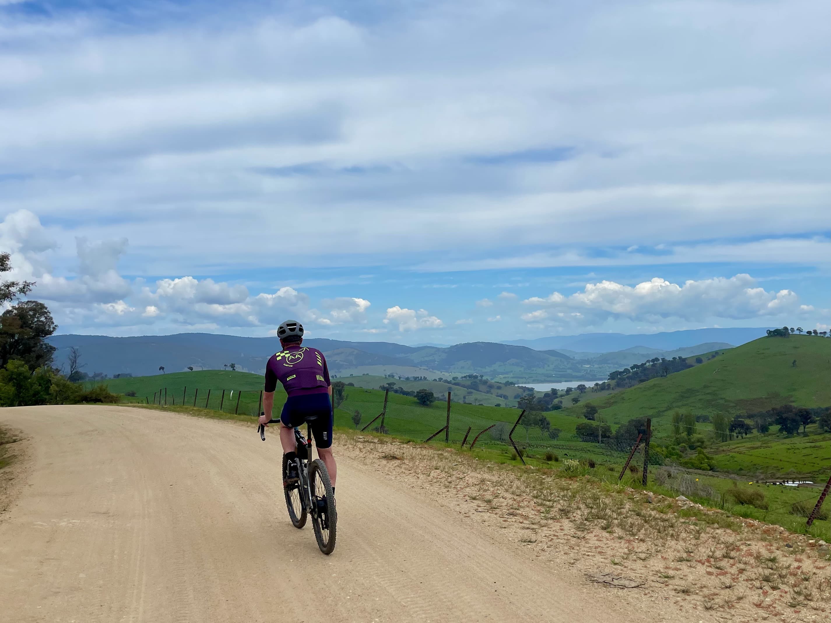 Cyclist riding on gravel road with expansive view of surrounding mountains and lake