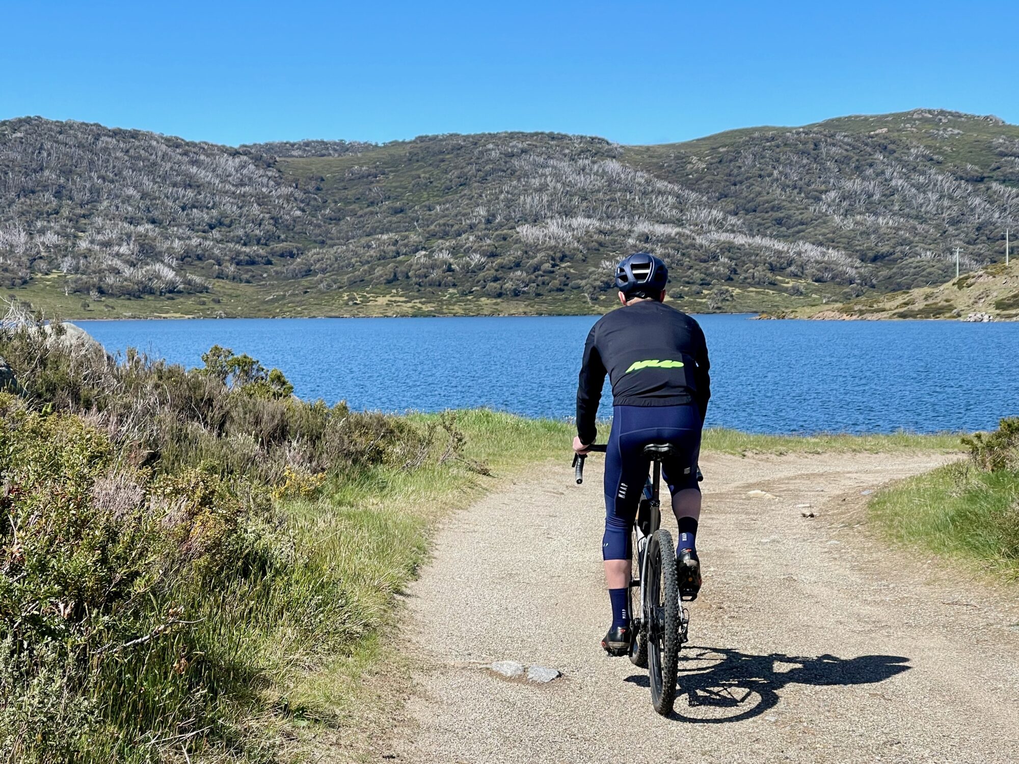 Cyclist riding on gravel road on a sunny day with a lake and mountain tops in the background 