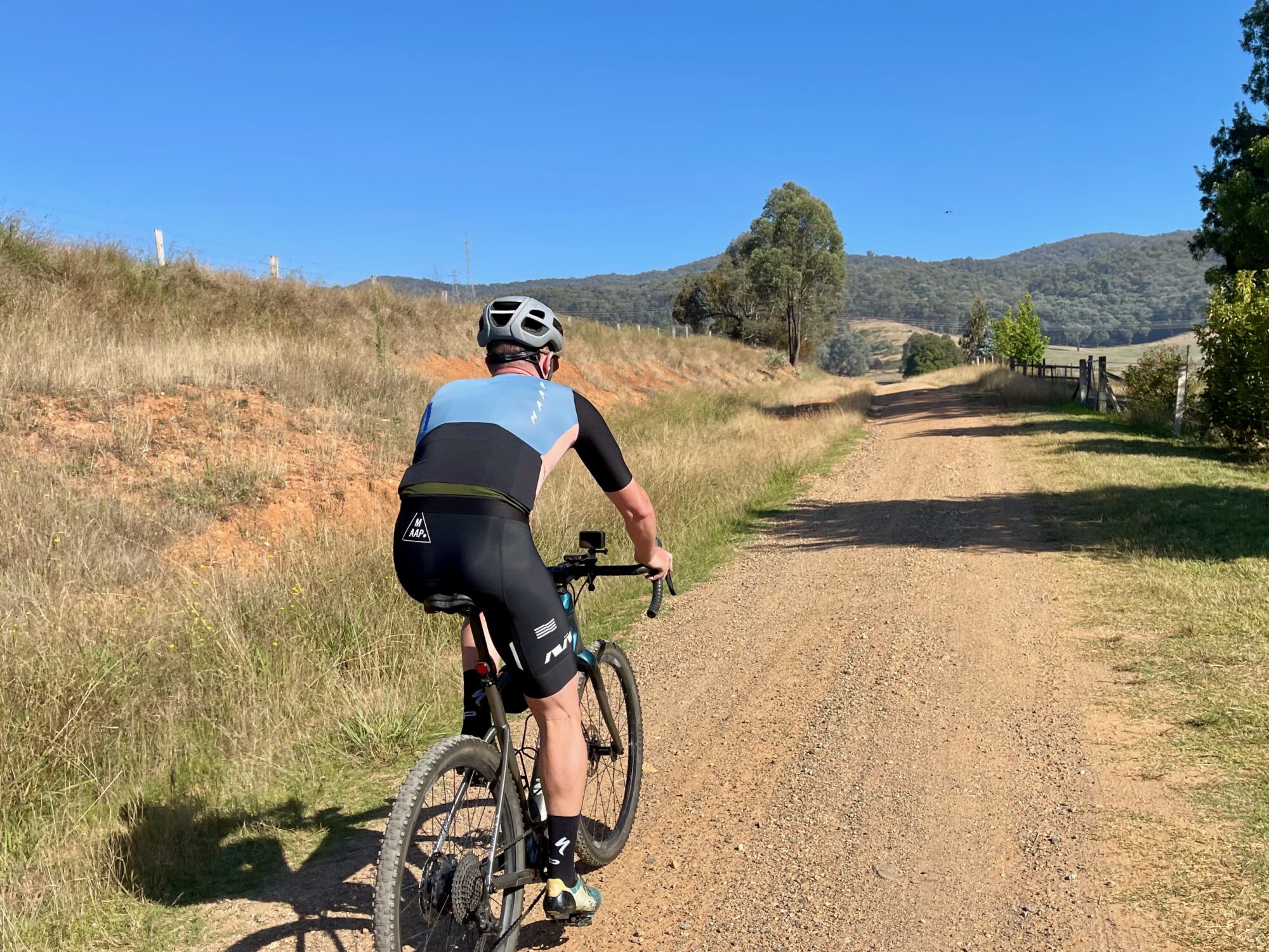 Cyclist riding on a gravel road through open farmland towards native bushland