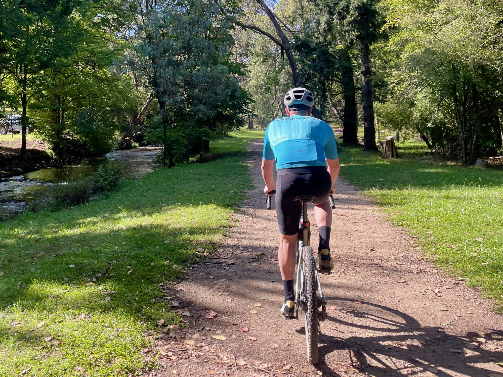 Cyclist riding along a smooth gravel track beside a river surrounded by trees 