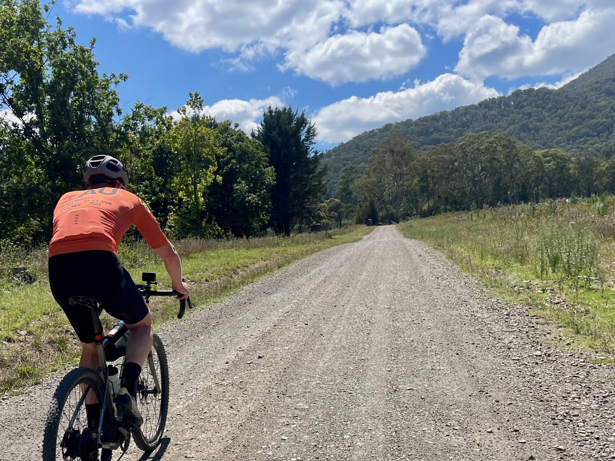 A cyclist riding on a gravel road with native bushland covered mountains in the background on a sunny day