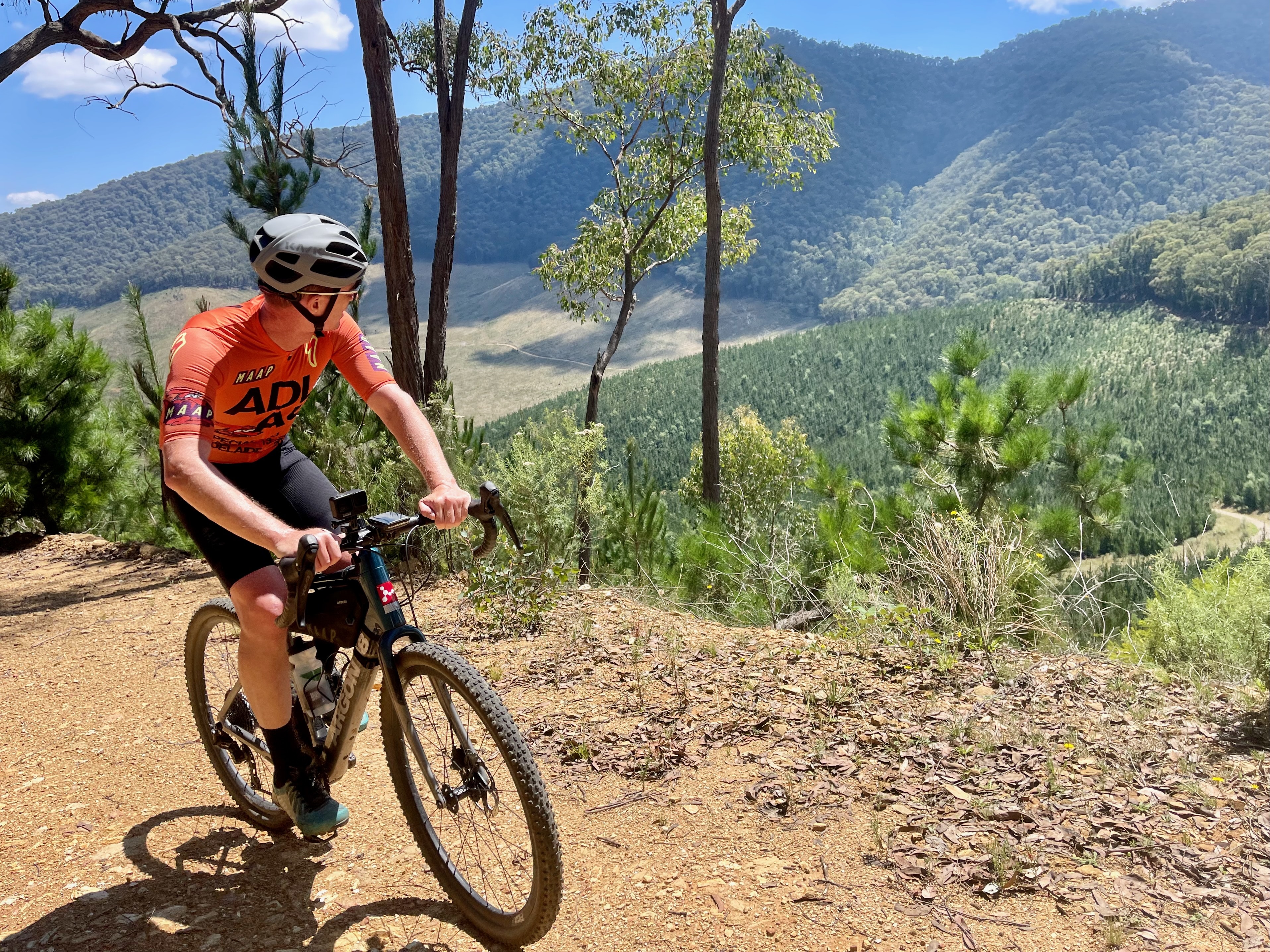 A cyclist climbing up a gravel road with views of tree covered valleys and mountains in the background