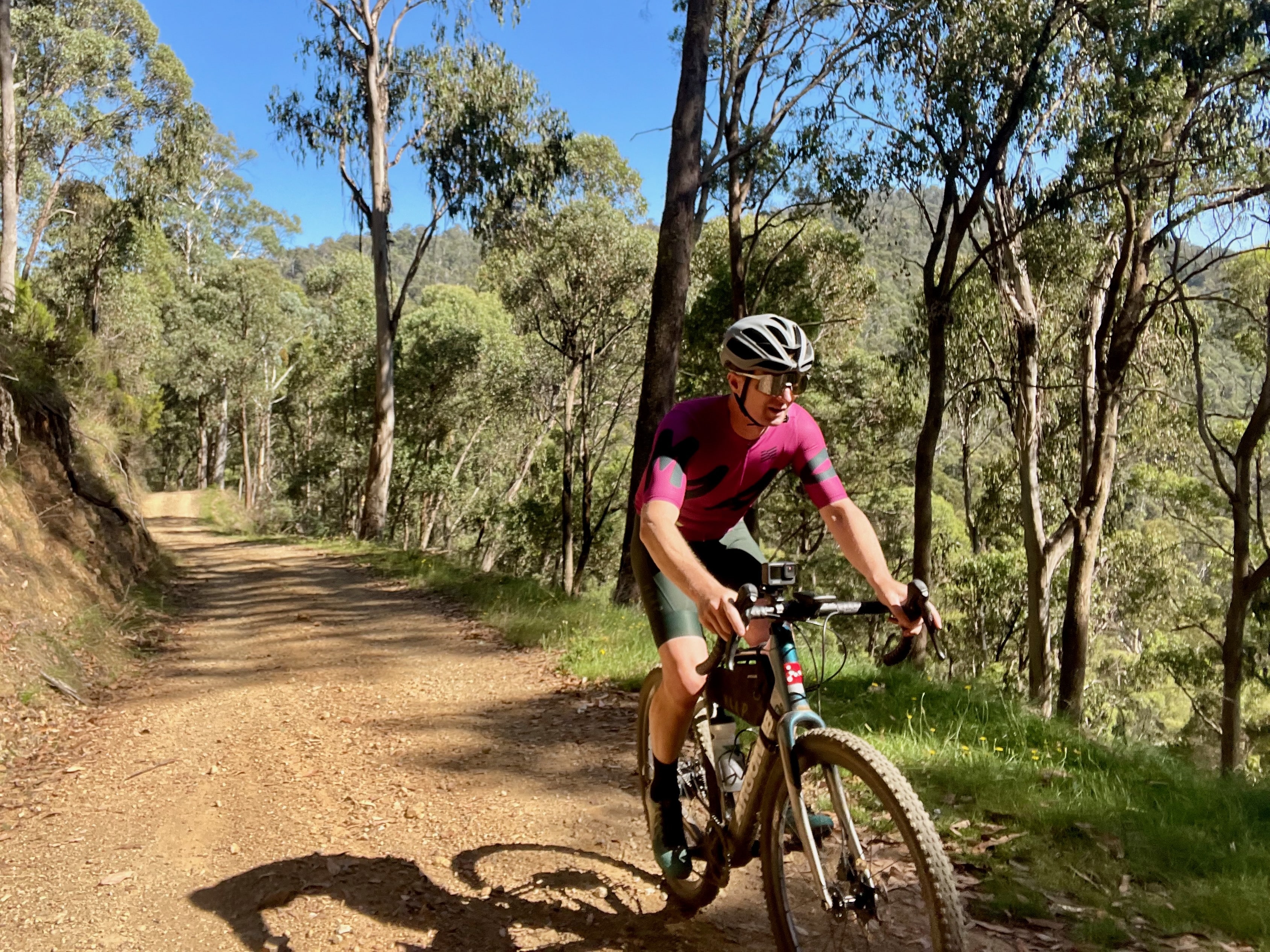 Two cyclists riding on a mountain gravel road through the forest on a sunny day