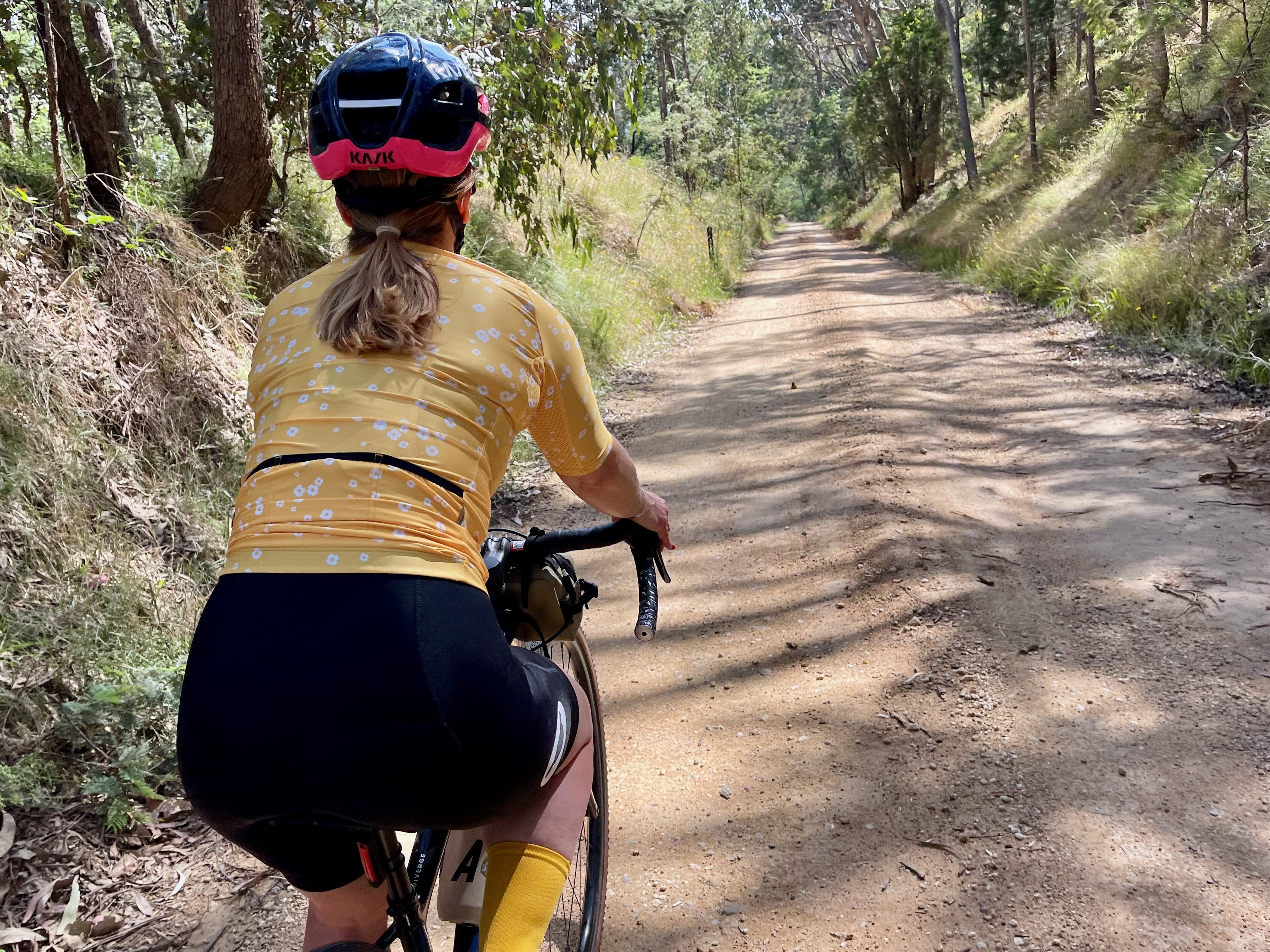A female cyclist riding down a gentle smooth gravel road surrounded by native bushland