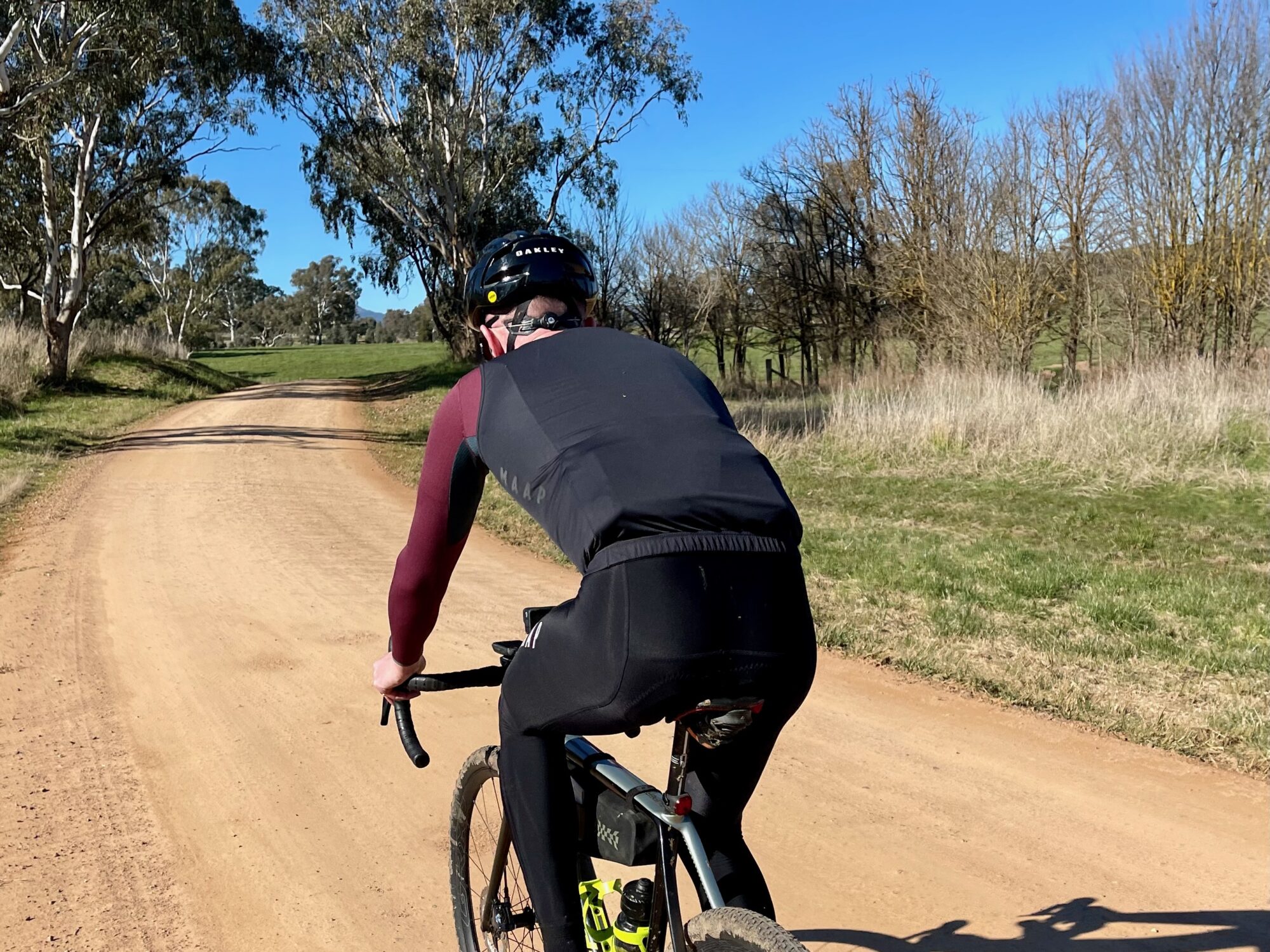 Cyclist riding on a winding smooth gravel road through open farmland on a sunny day 