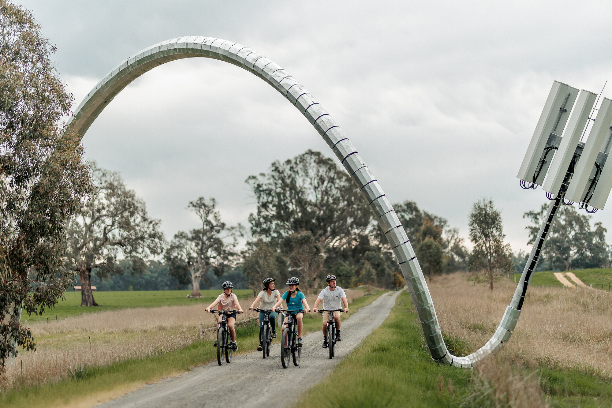 A family of four cycling over a pedestrian bridge over a lake surrounded by hills on an overcast day