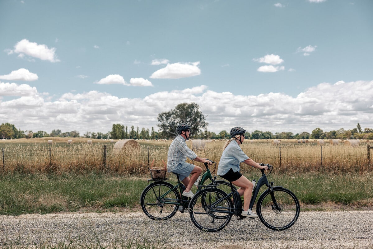 Two cyclists ride past a field of hay bales, along a path