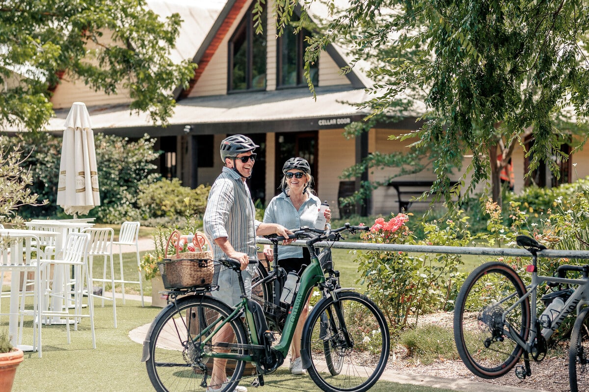 Two cyclists parking their bikes in a leafy courtyard by a cellar door.