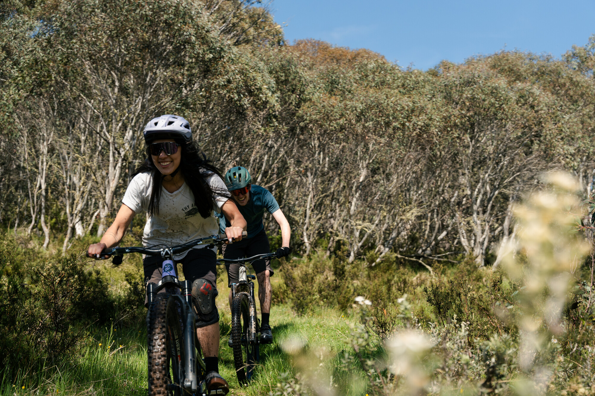 Two cyclists smiling as they ride through native bushland at Dinner Plains Mountain Bike Park