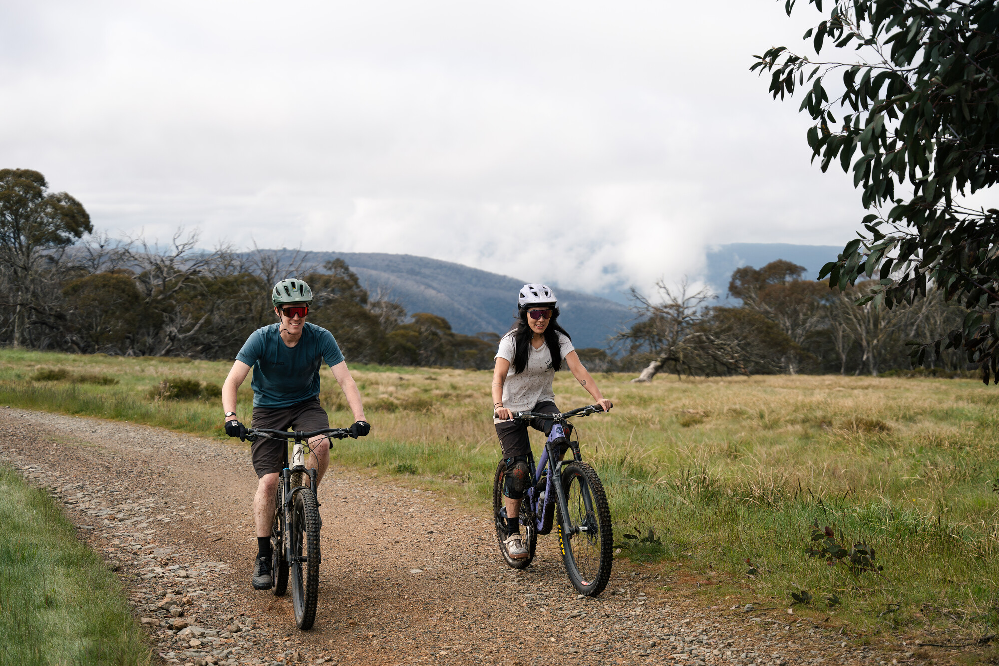 Two cyclists smiling as they ride through native bushland at Dinner Plains Mountain Bike Park