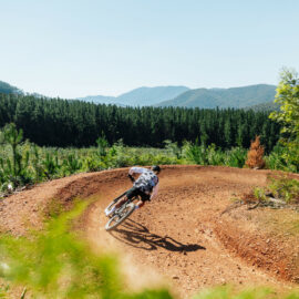 Cyclist riding around a berm at Mystic Bike Park with views of mountains