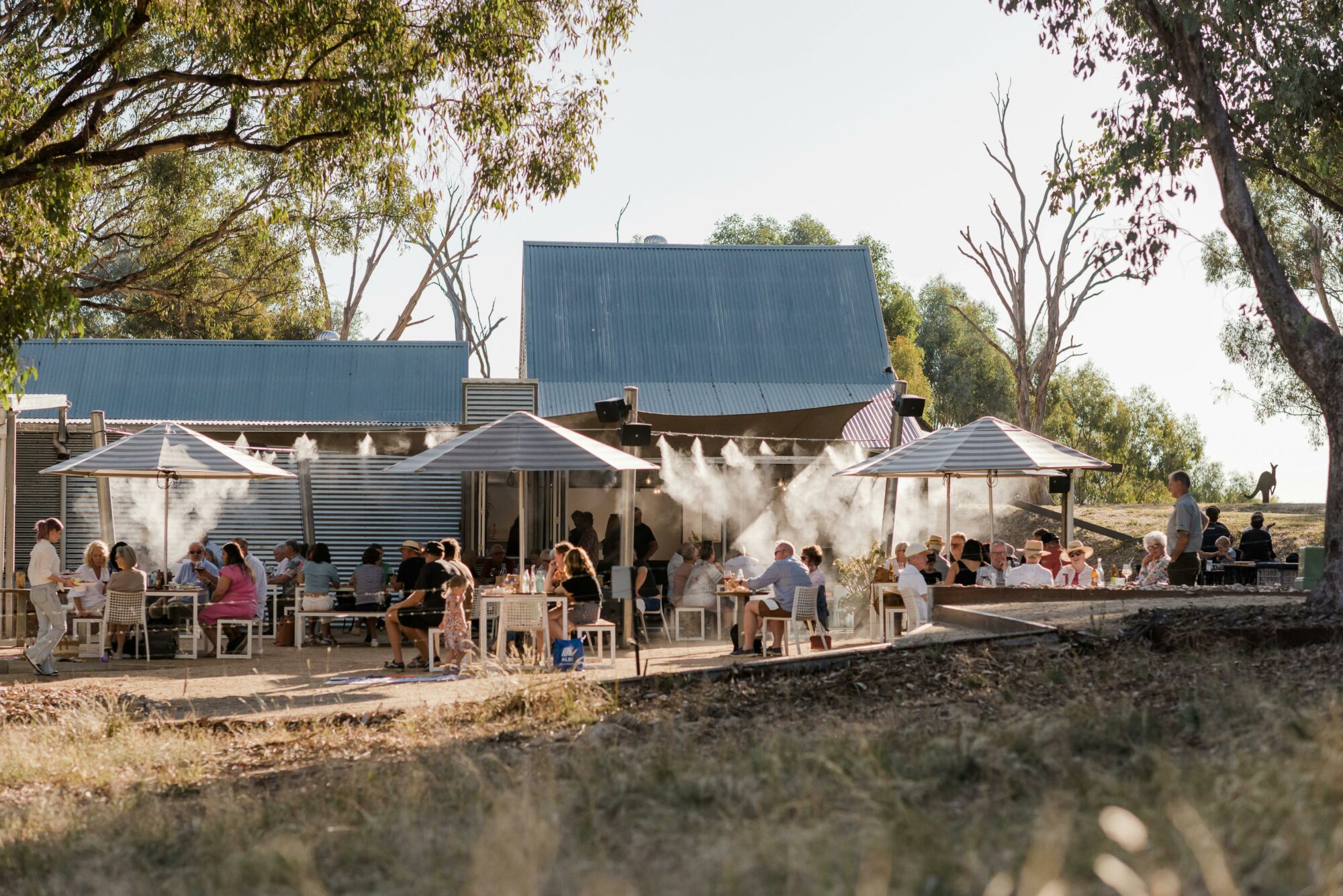 Crowd under umbrellas next to winery shed