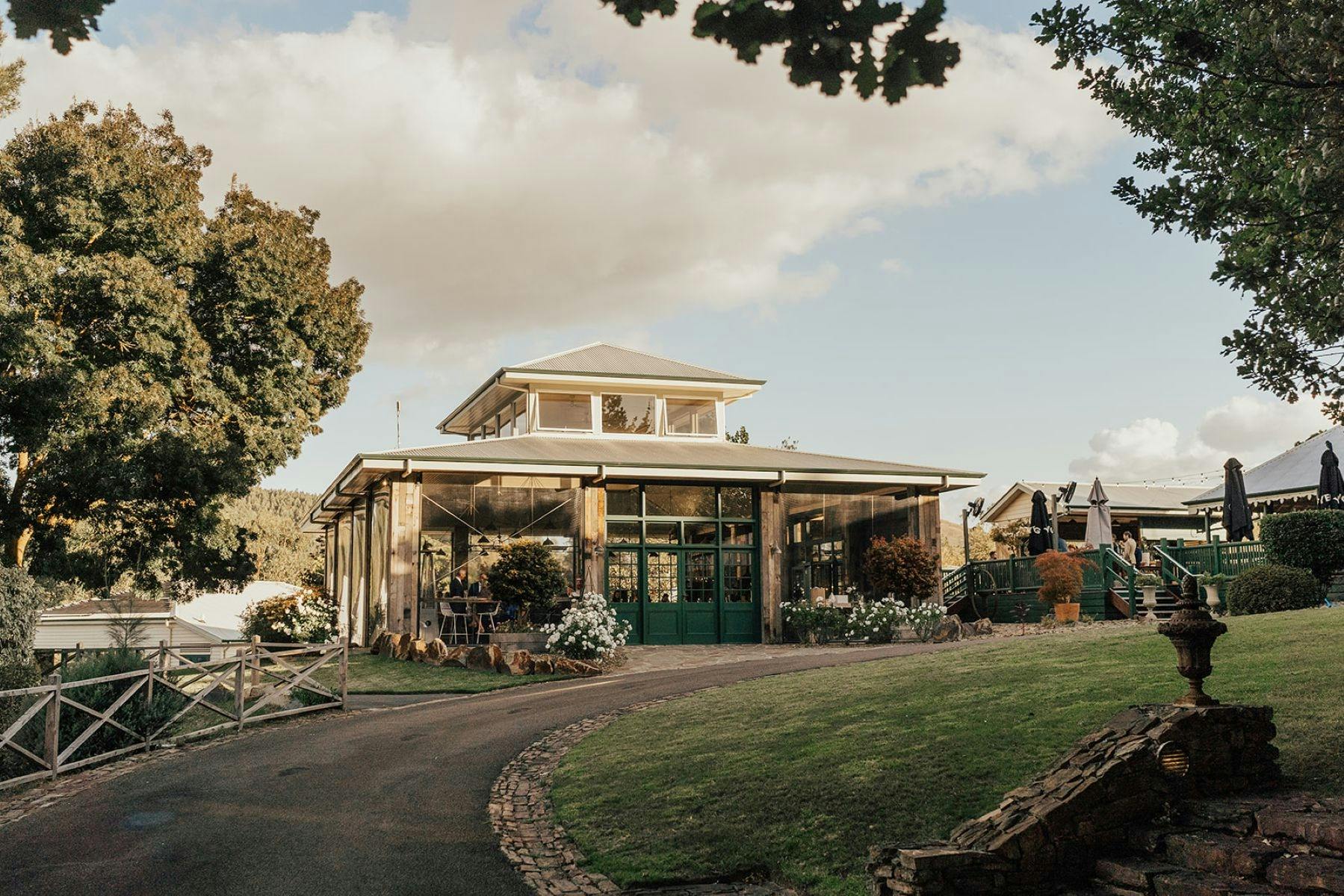 A square building used for events with tall timber beams and lush bushes surrounding