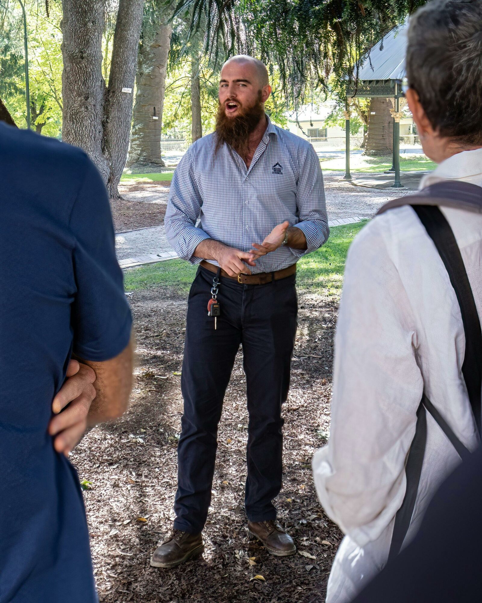 Tour guide speaking to two people in garden, large trees in background