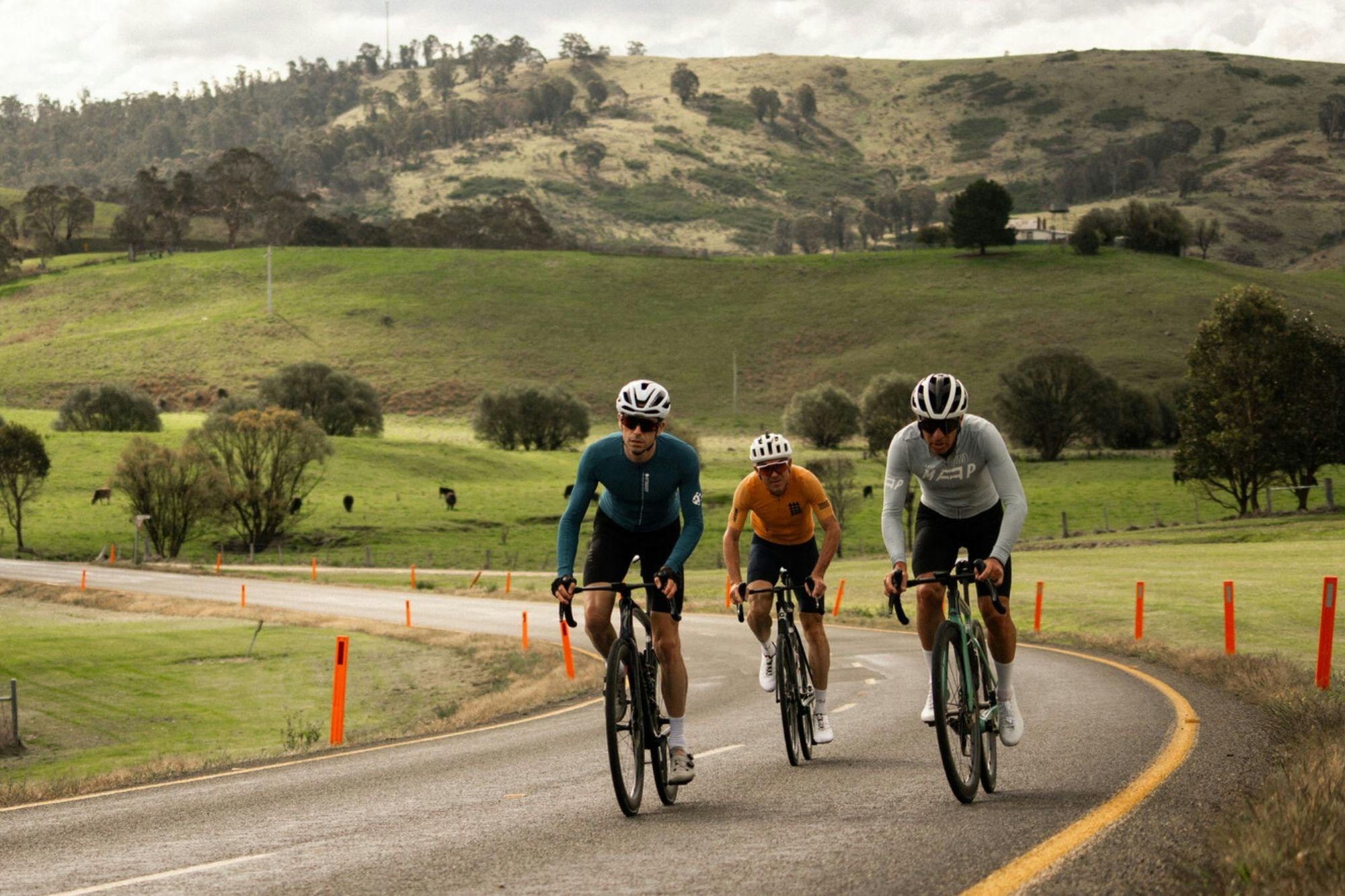 Three cyclists riding the Dinner Plain 7 Peaks Challenge ride past rolling green hills.