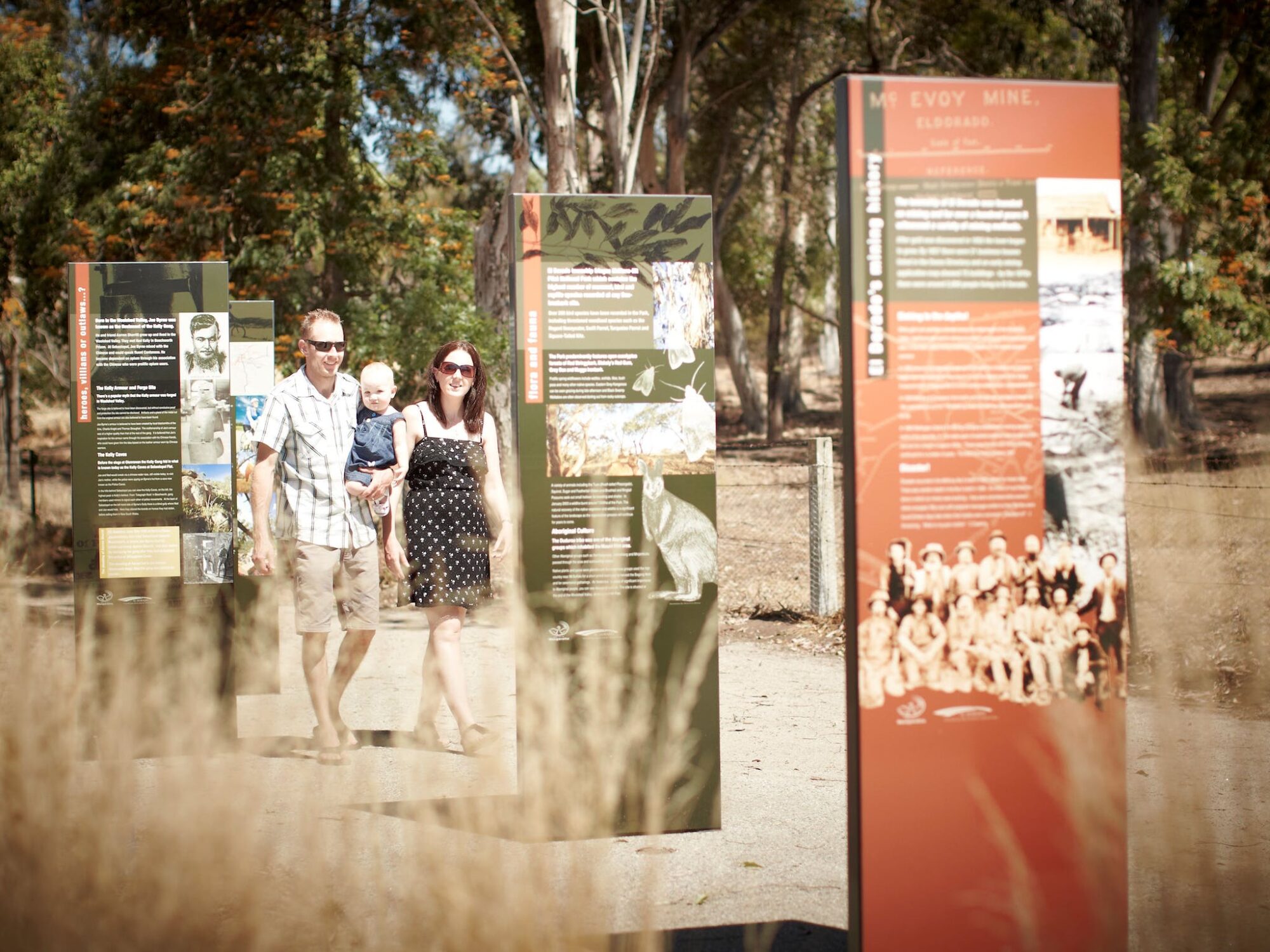 Family walking along path in the sun, looking at interpretive signage