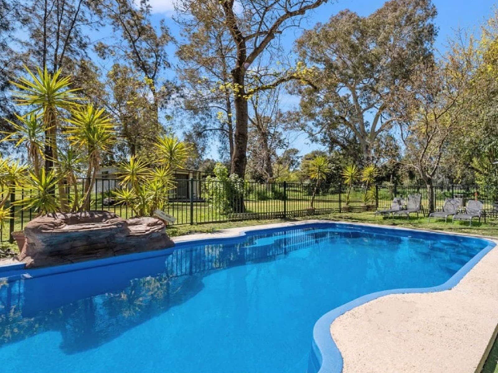 Pool on site with a gate around, lounge chairs and trees