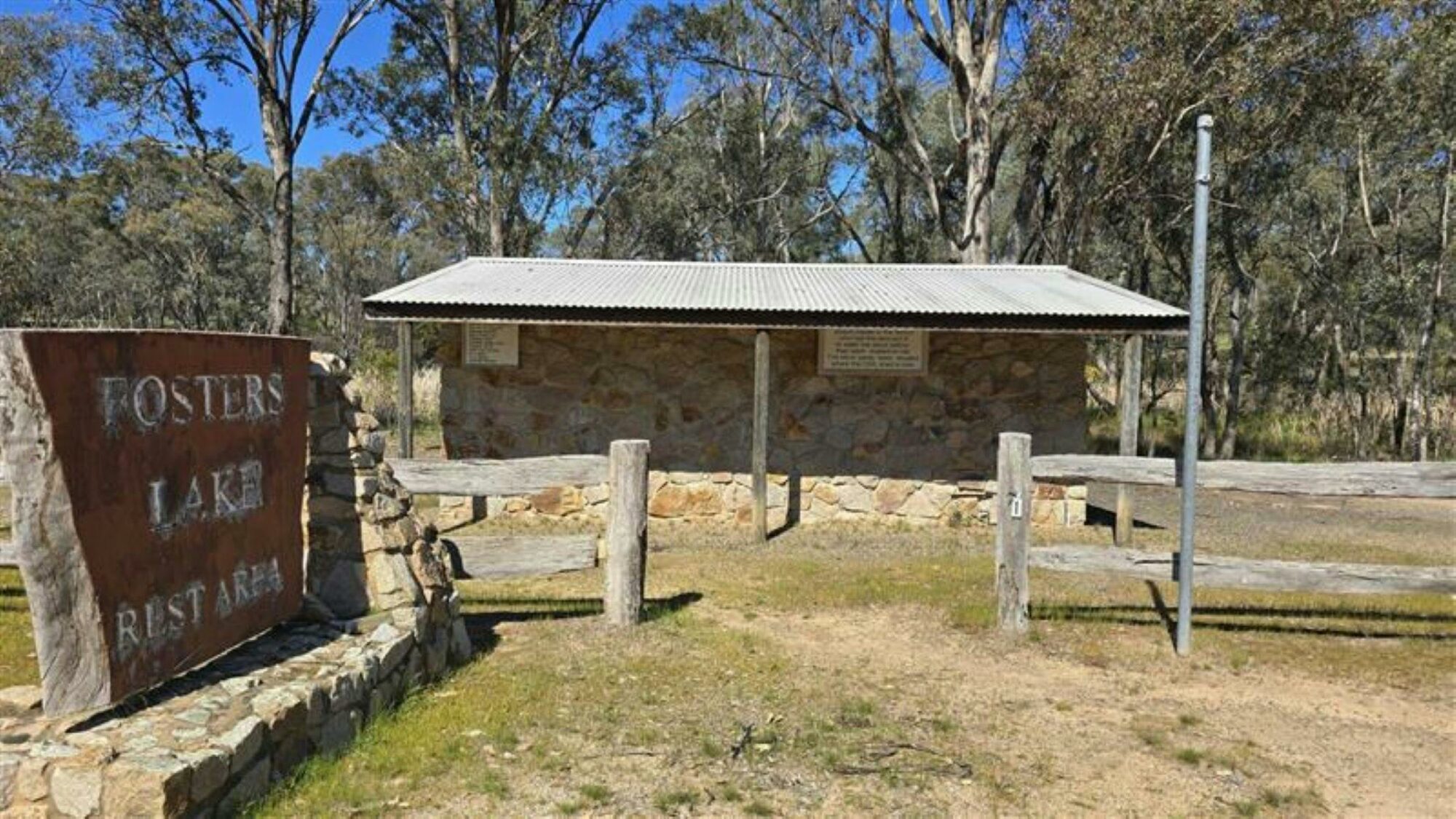 Stone building with wooden fence. Rustic sign saying Fosters Lake Rest Area built on a stone ledge