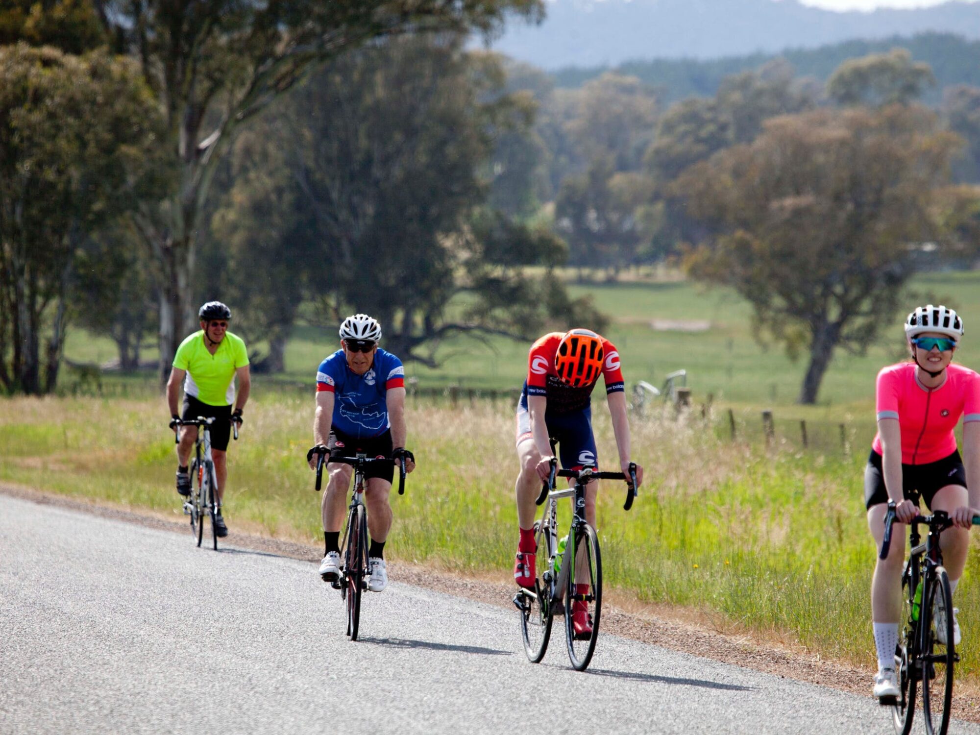 cyclists riding on the road farm land and hills in the background near glenrowan
