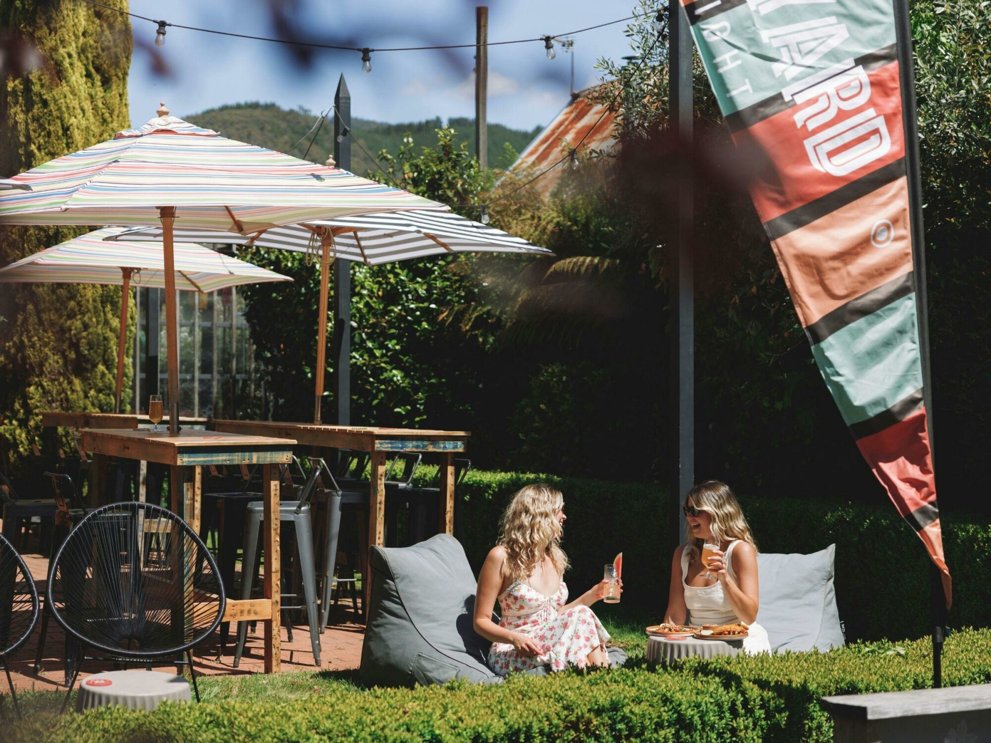 Two women sitting in the sun on beanbags on the front lawn of The Yard Bright enjoying drinks