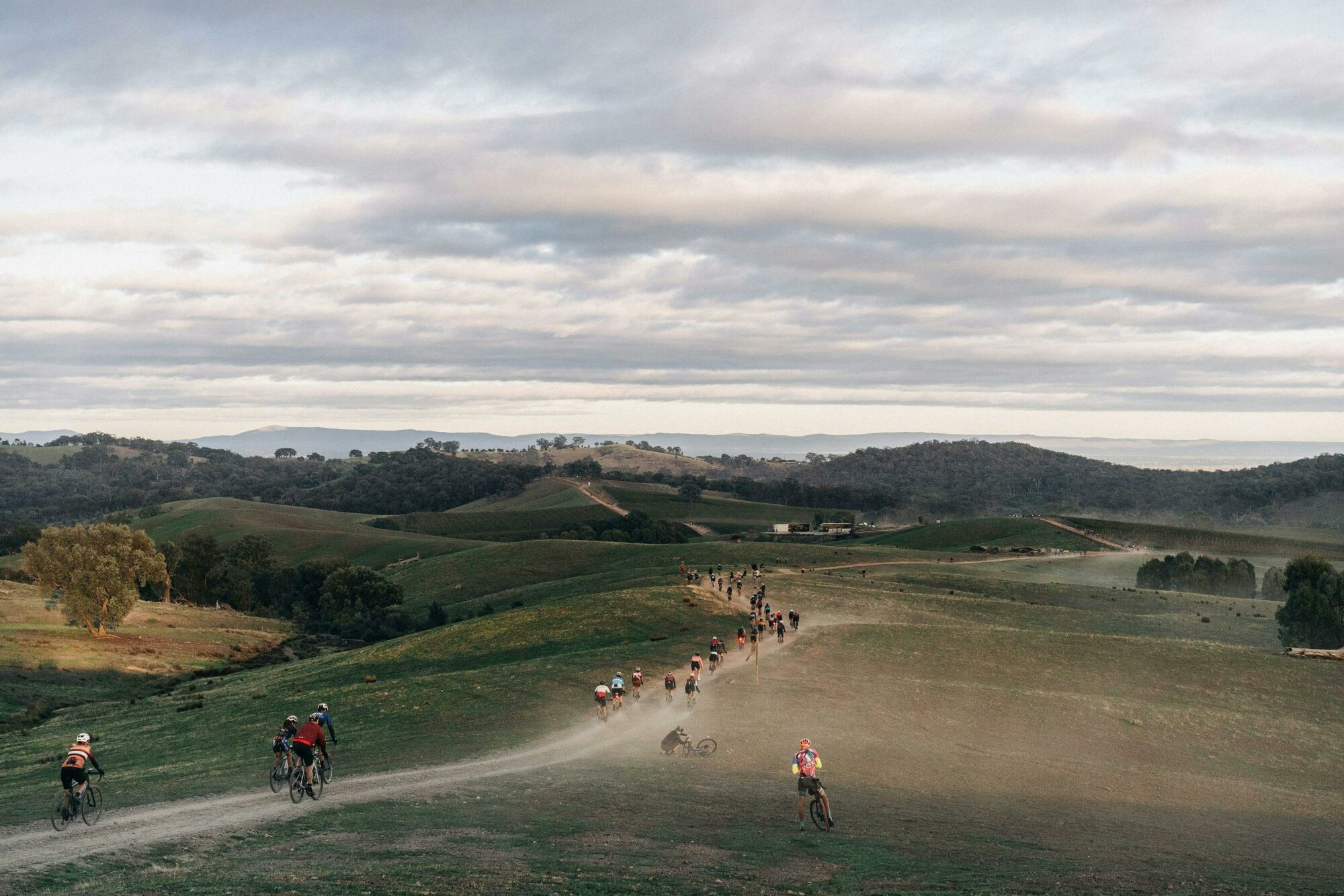 Landscape view of cyclists on gravel path riding among rolling hills.
