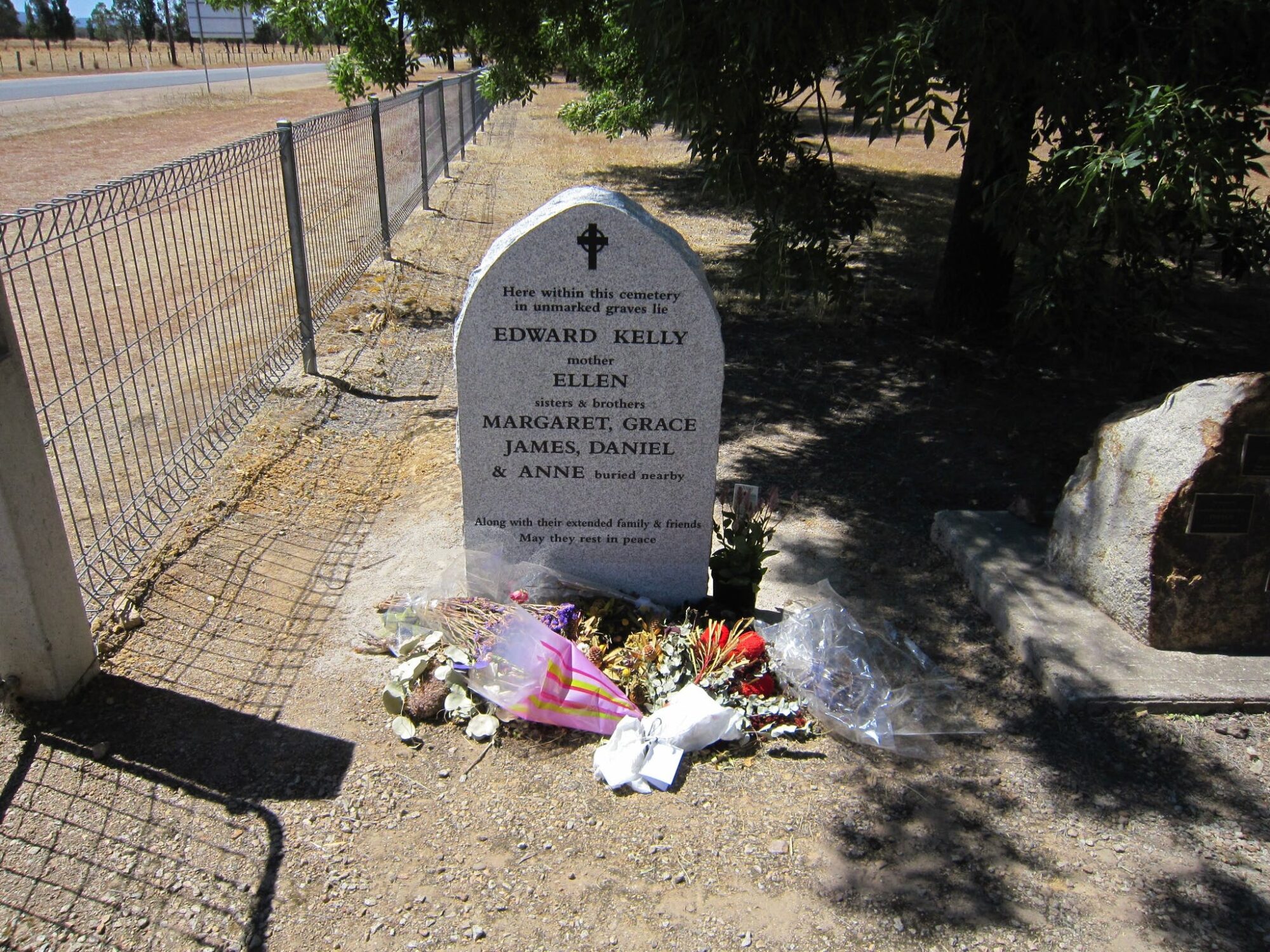 Kelly Family Headstone beside gate at entry to Greta Cemetery, flowers,  shadows, wire fence, tree