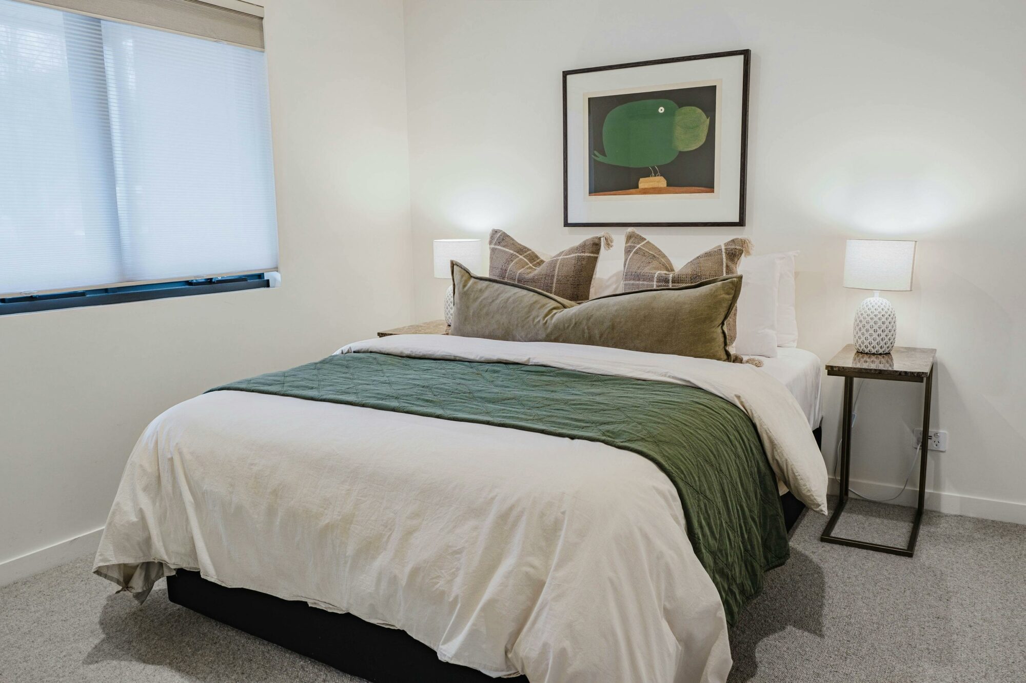 Bedroom with bed, tableside lamp and a painting on the wall