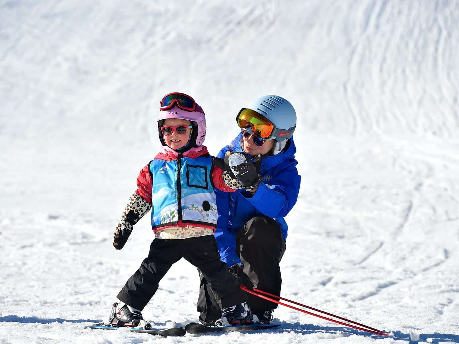 child being taught how to ski by instructor
