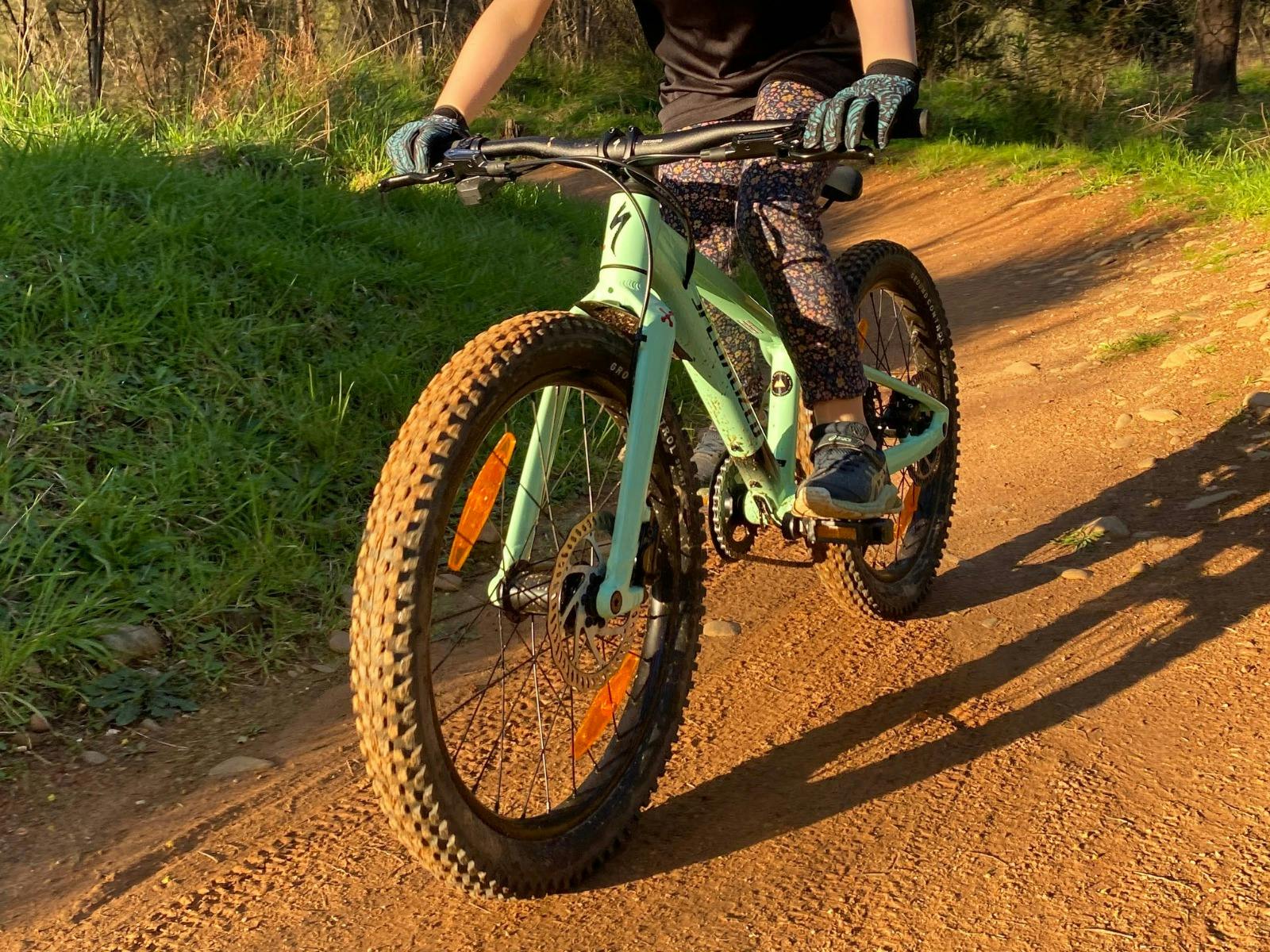 A child on a green bike rides on a brown trail.