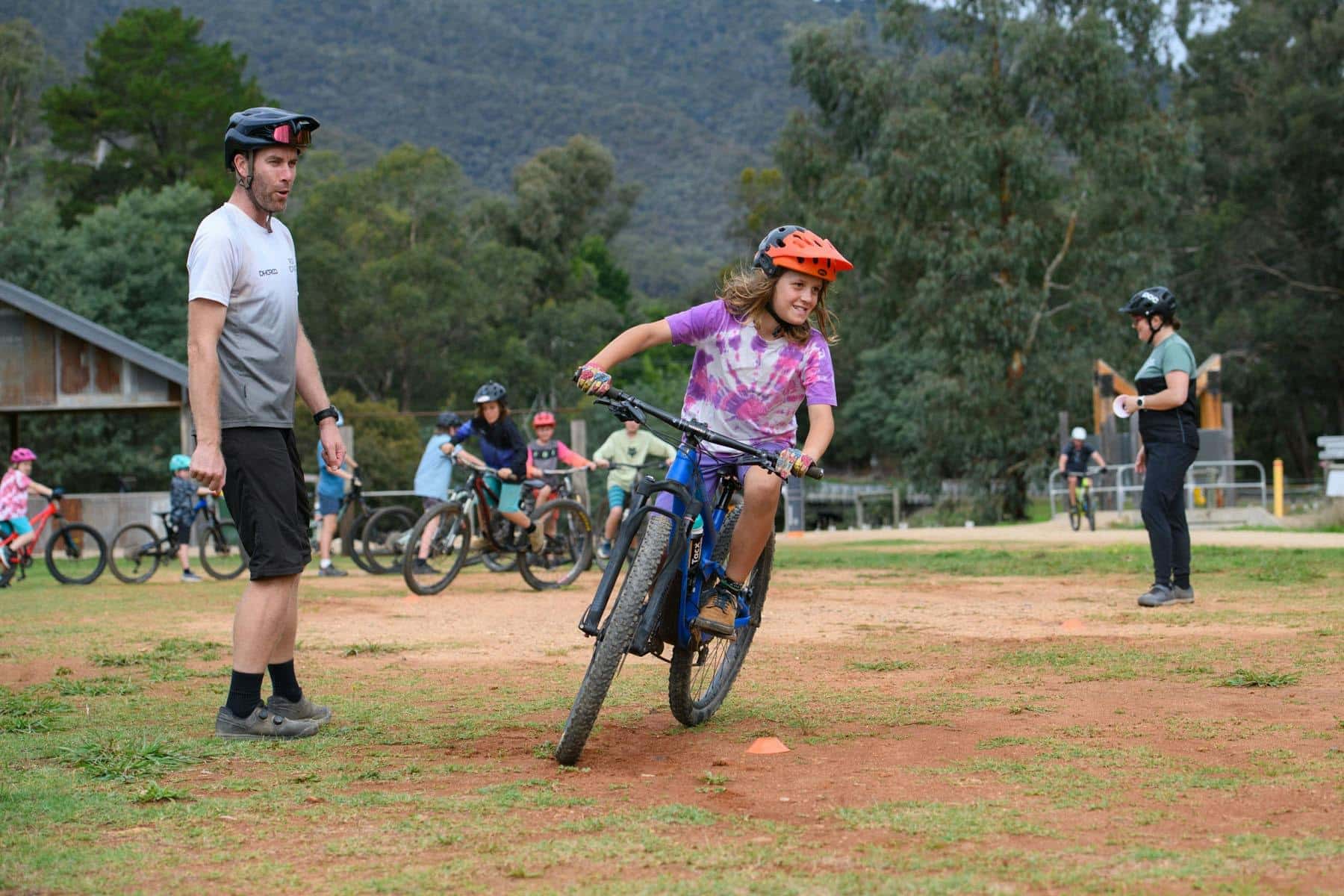 A coach stands watching a young rider on his bike