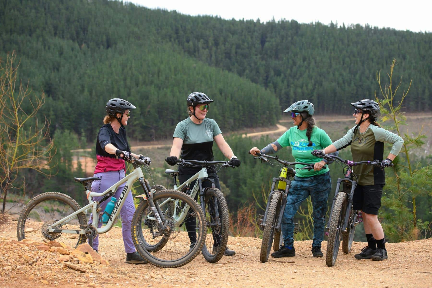 A coach with a bike stands facing a group of female riders