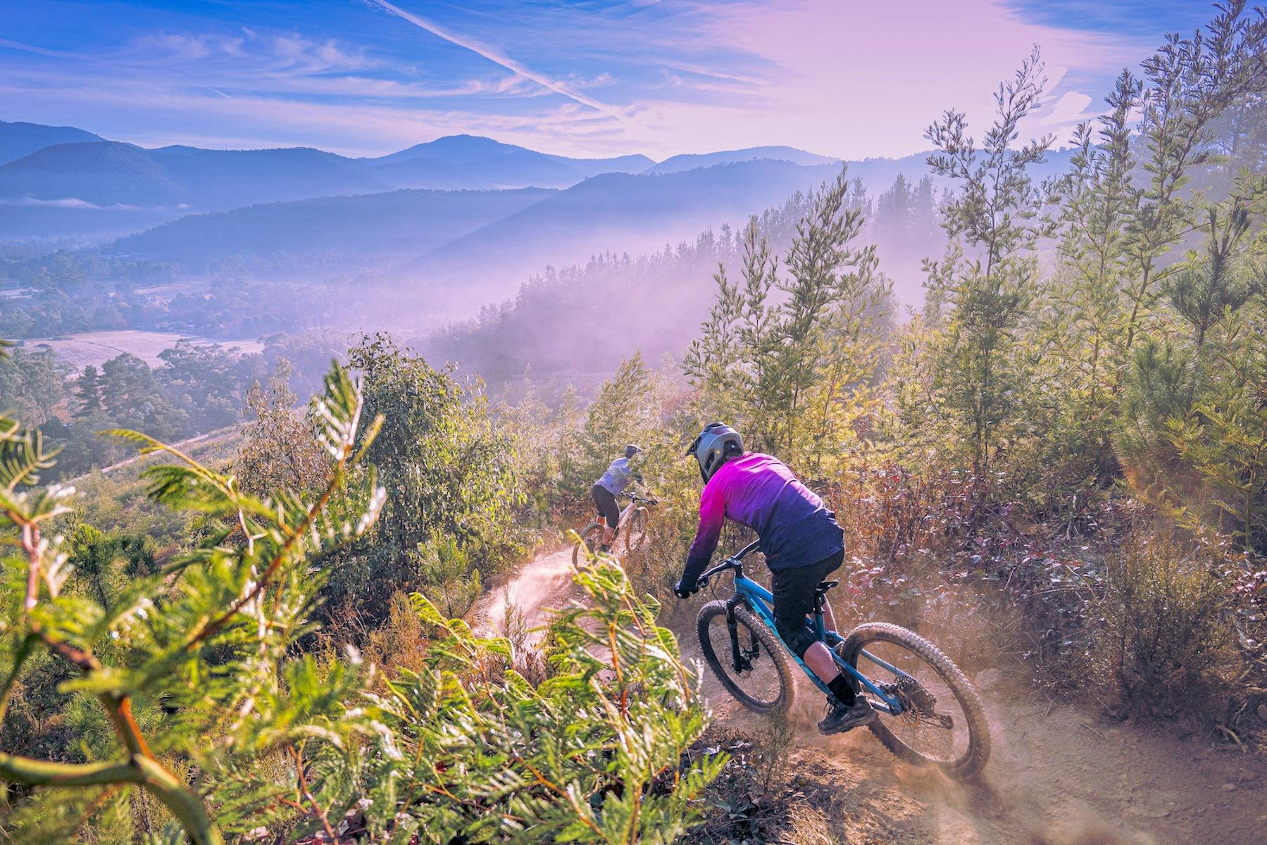 Two riders head down a mountain on their mountain bikes under a blue sky.