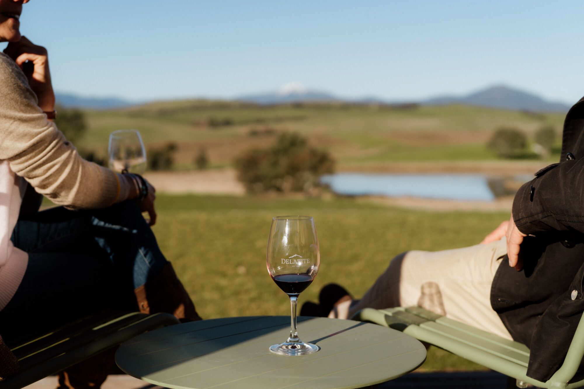 A glass of wine with two people on either side, with Mt Buller in the background