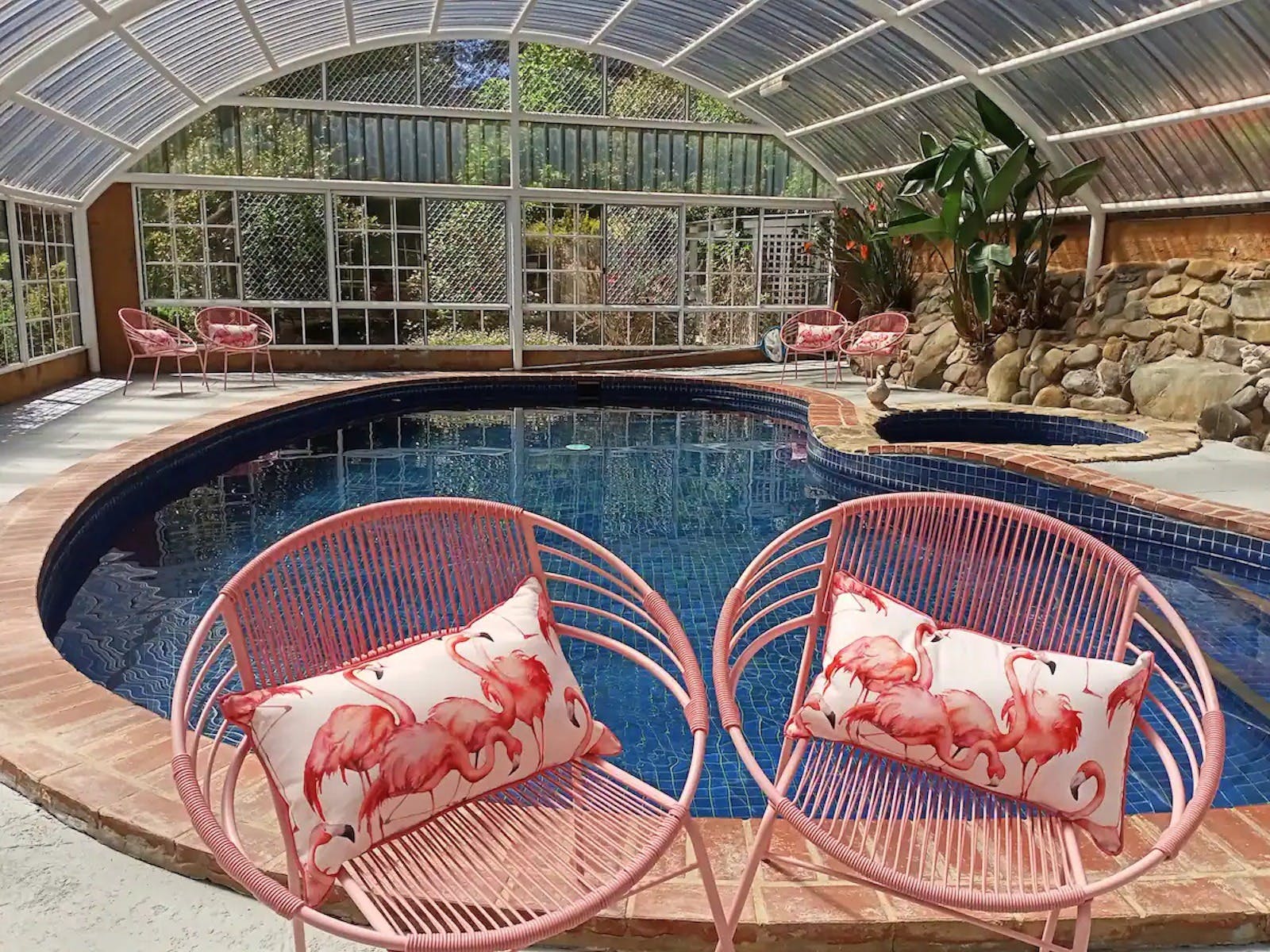 Two pink chairs sit in front of a blue pool under a clear domed roof.