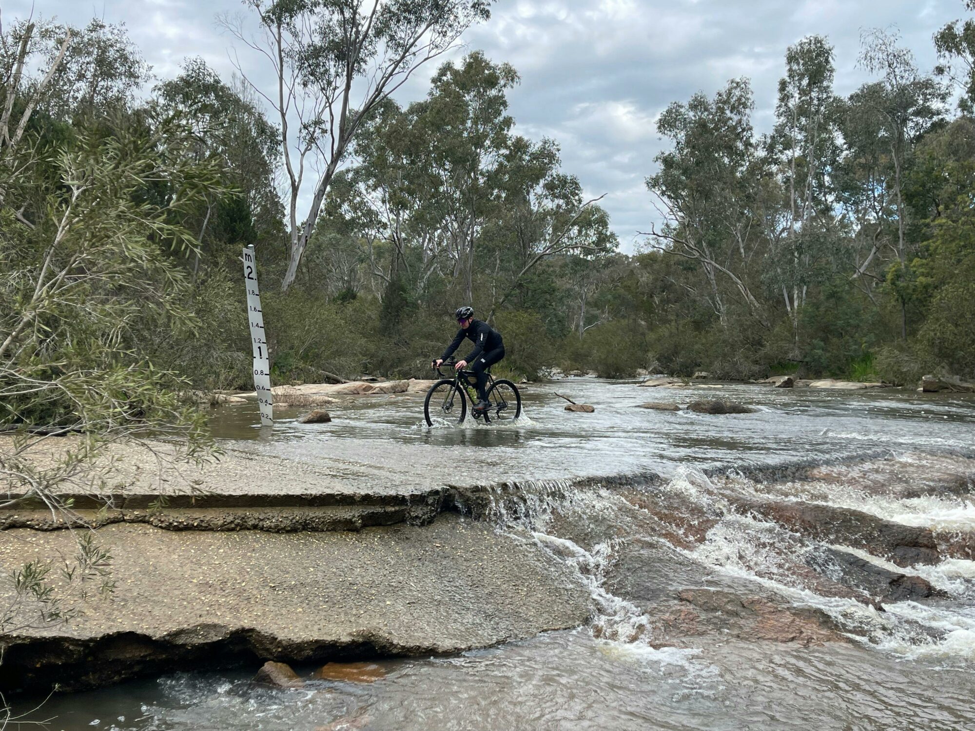 Cyclist on cement bridge going through creek, flowing creek in foreground, trees