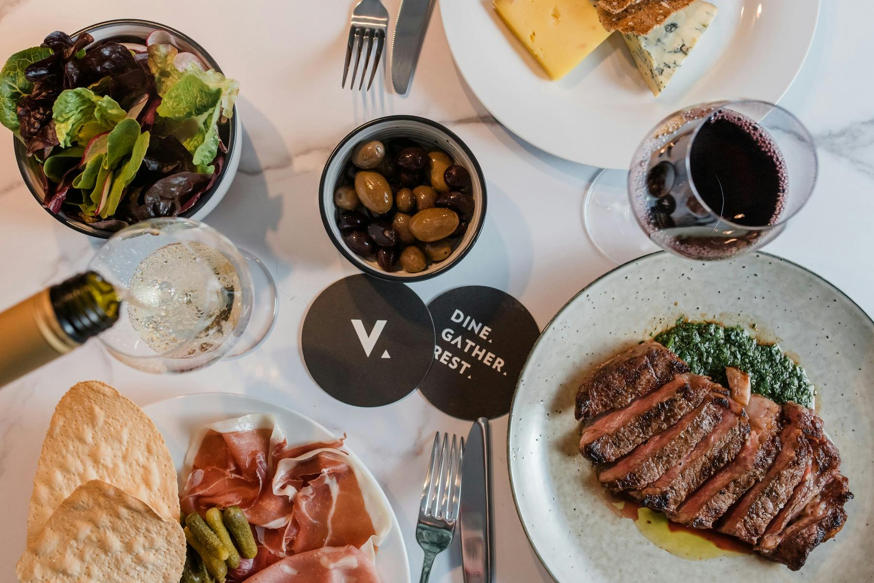 Steak, shaing plates and wine served on a white table