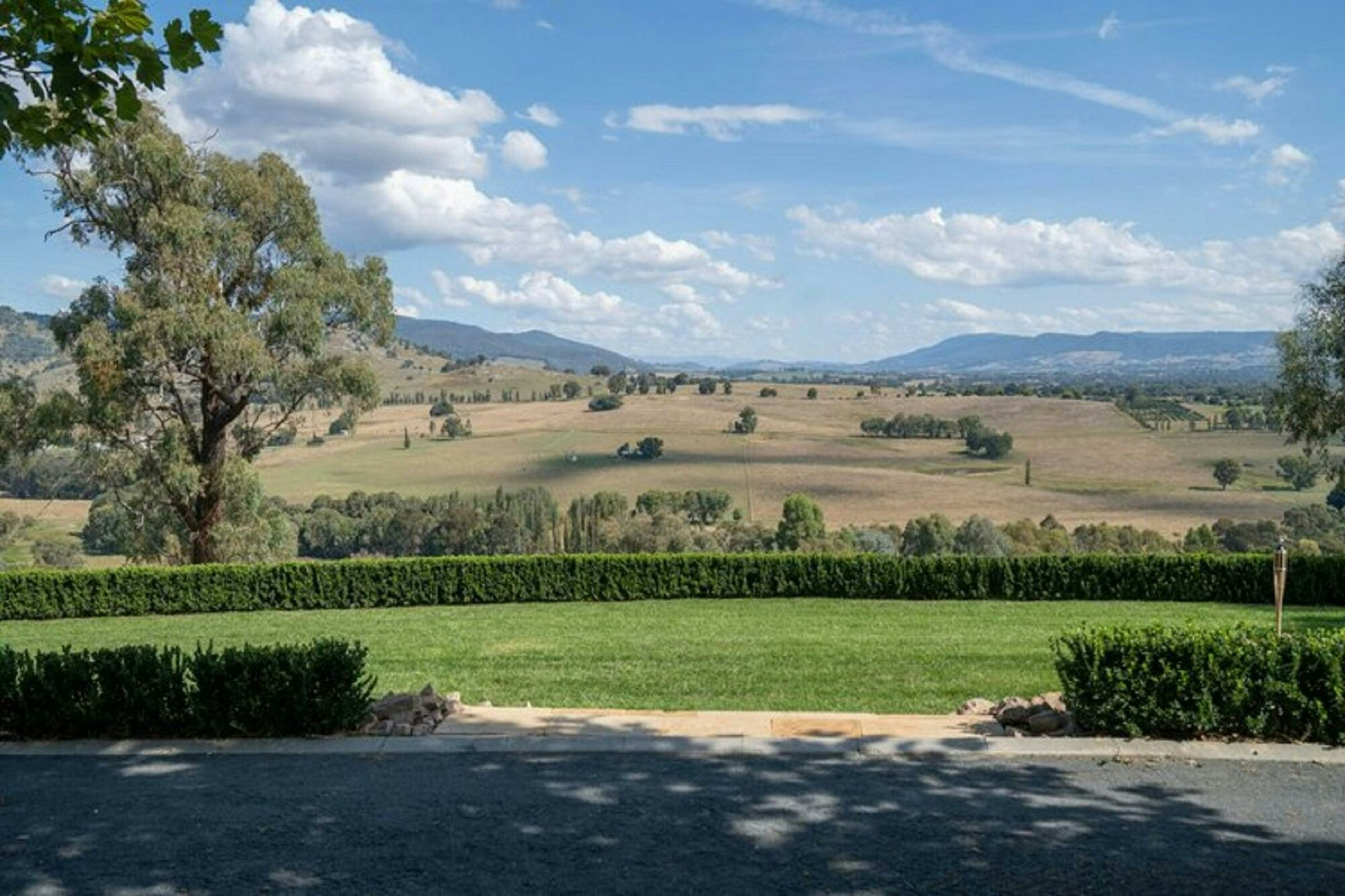 View overlooking green  lawns with the mountains in the background. The sky is blue with clouds