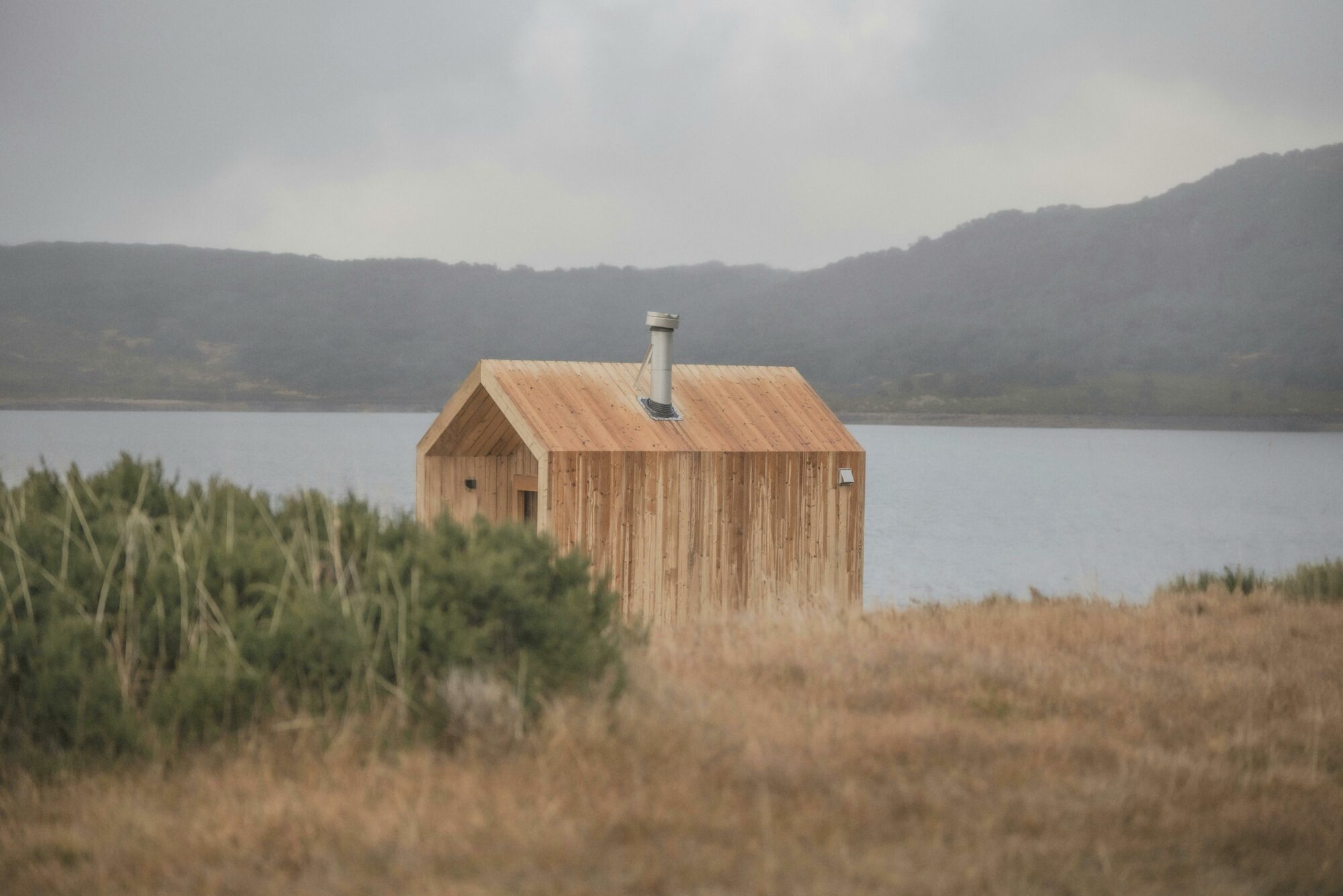 Nature shot of light coloured wood sauna  with chimney on lake in the mountains