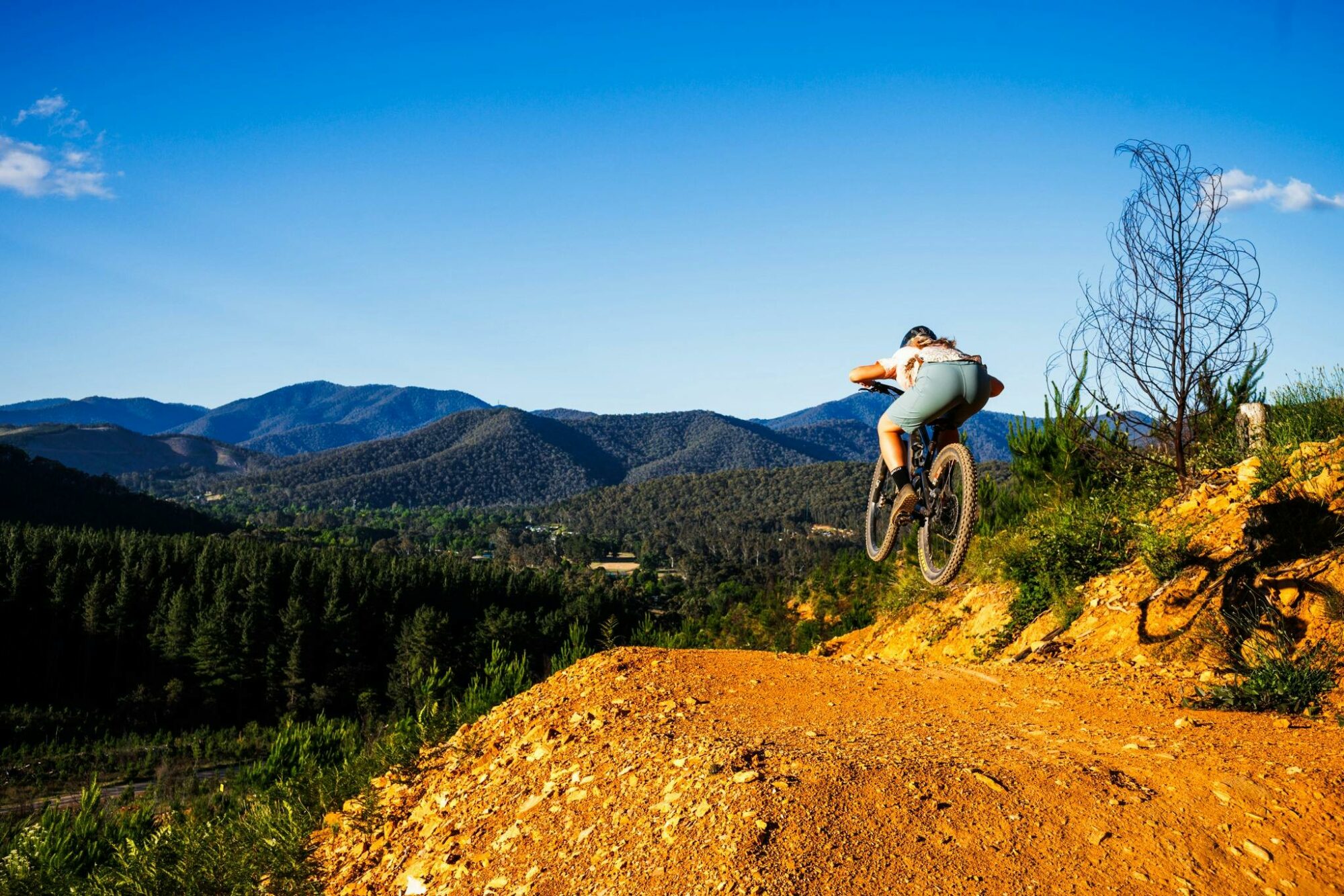 MTB riders doing a jump with mtb bike with mountains in the backdrop