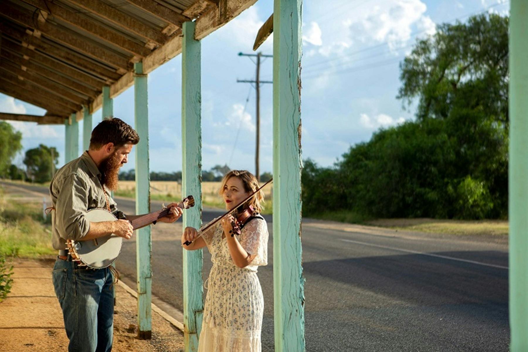 Man plays banjo and woman plays violin ourside old building