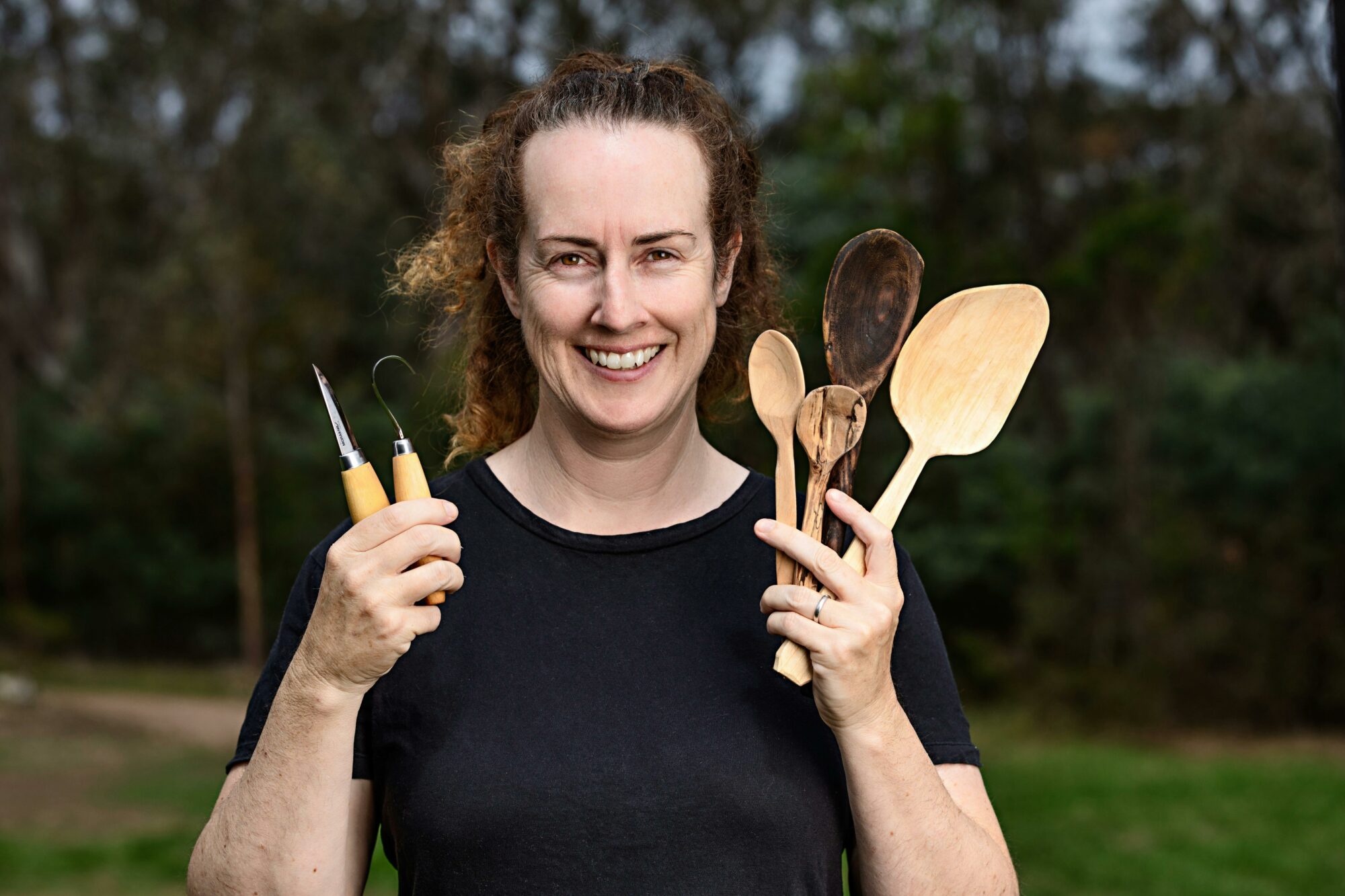 Workshop facilitar Nat Ord holding up spoons and carving tools smiling