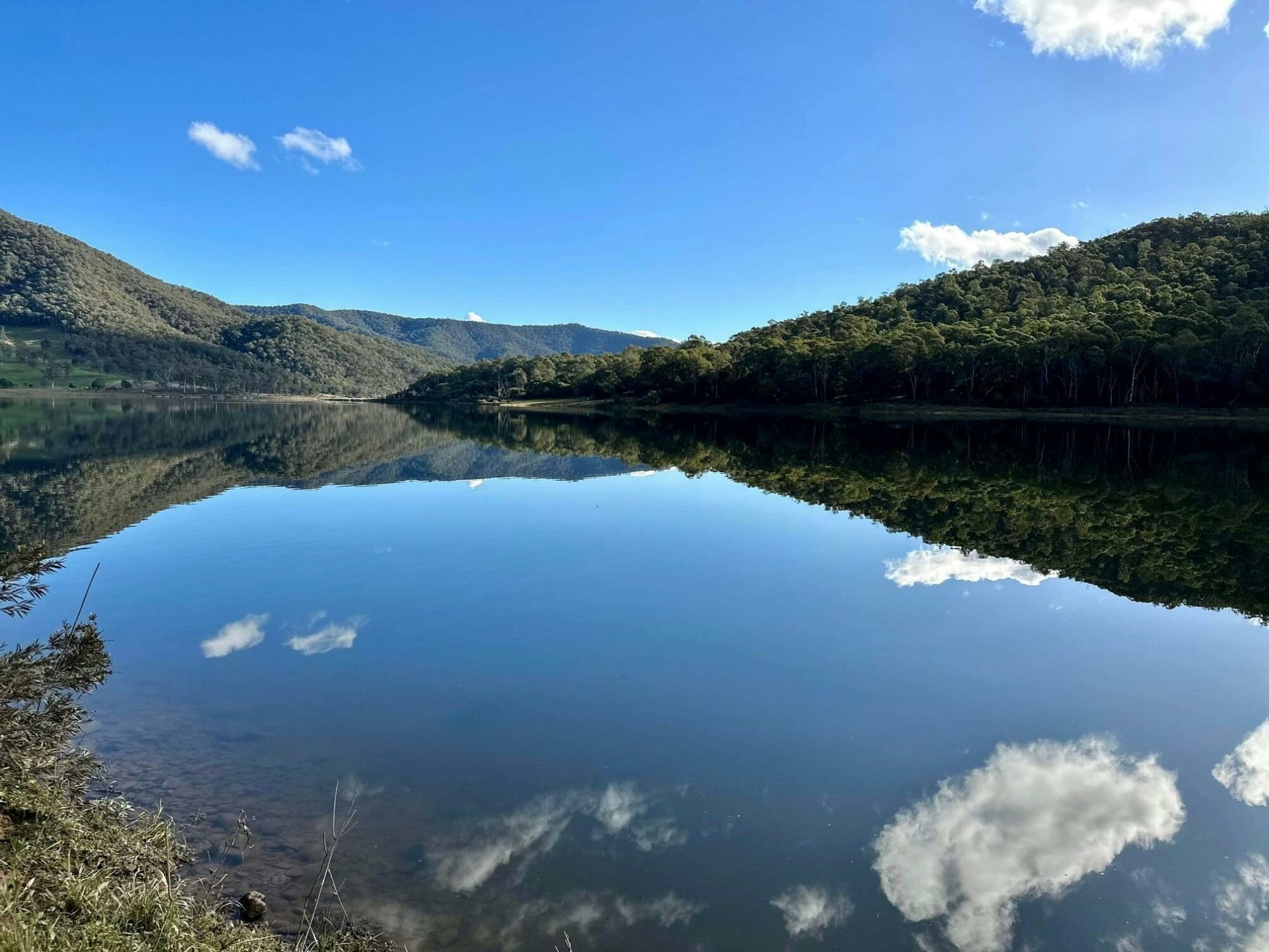 The glassy water of the Dartmouth Dam on a blue sky day.